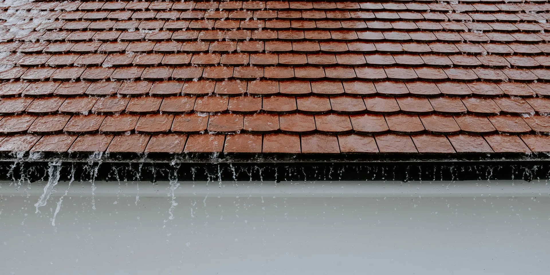 Rain running off a tiled roof into a white gutter