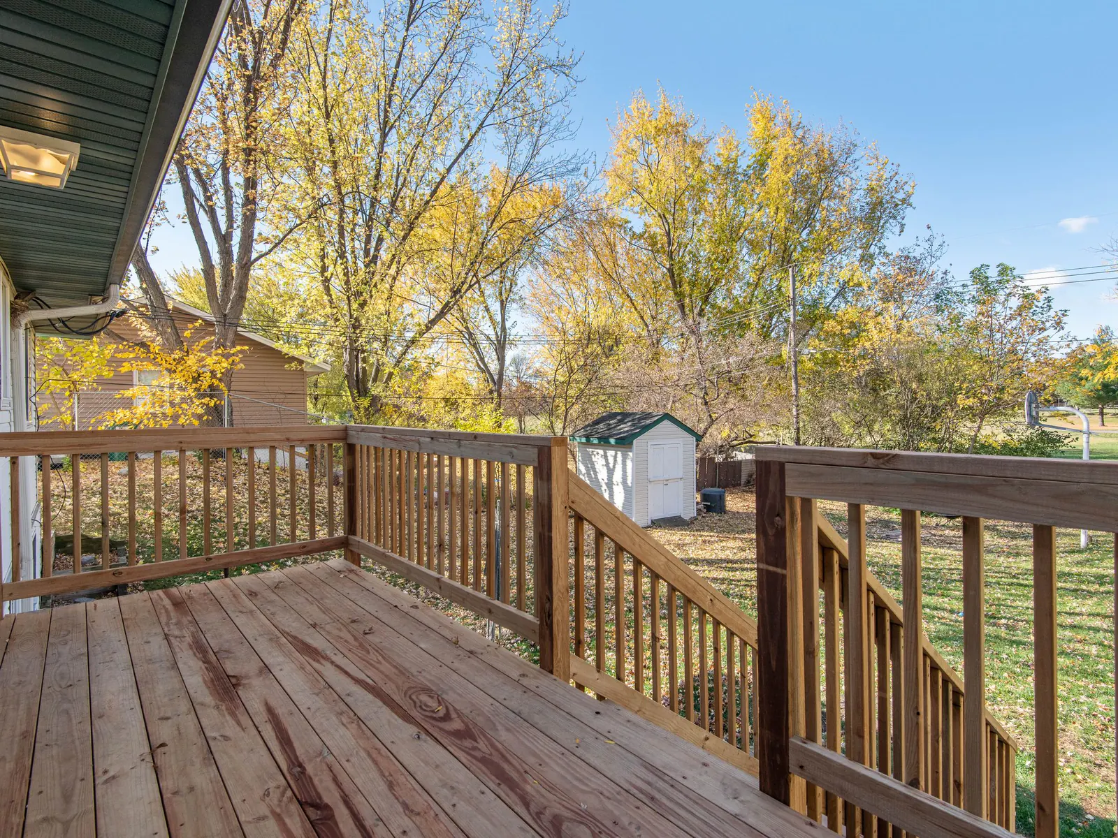 A wood deck with railings looking out on a yard of trees in fall color