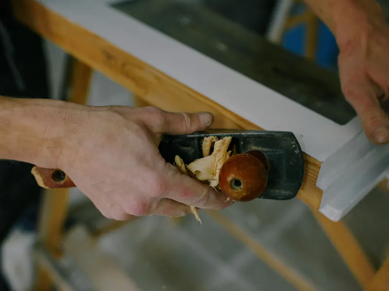A hand plane shaving a white window frame