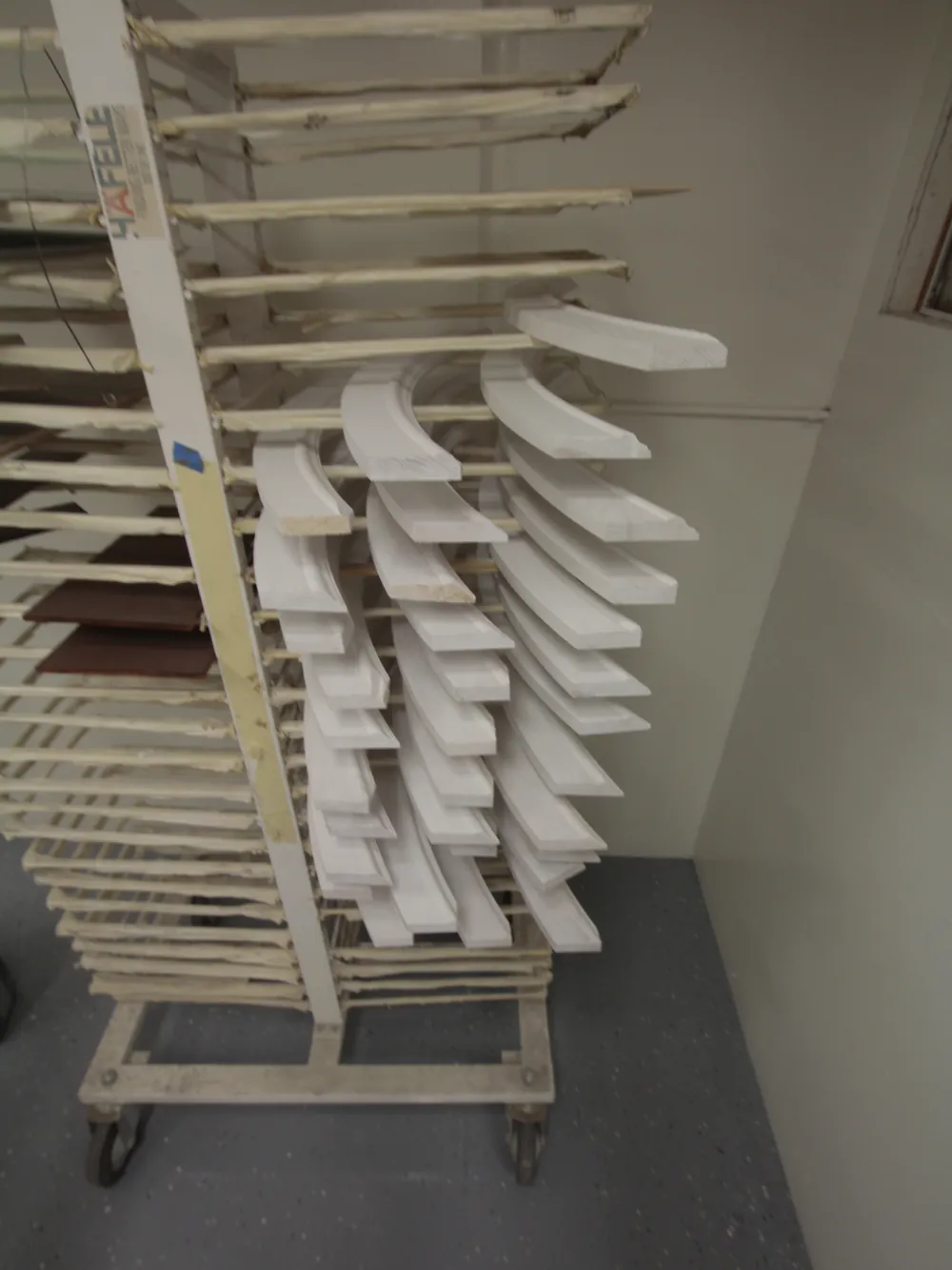 Freshly sprayed white trim and cabinet pieces drying on a rolling shop rack