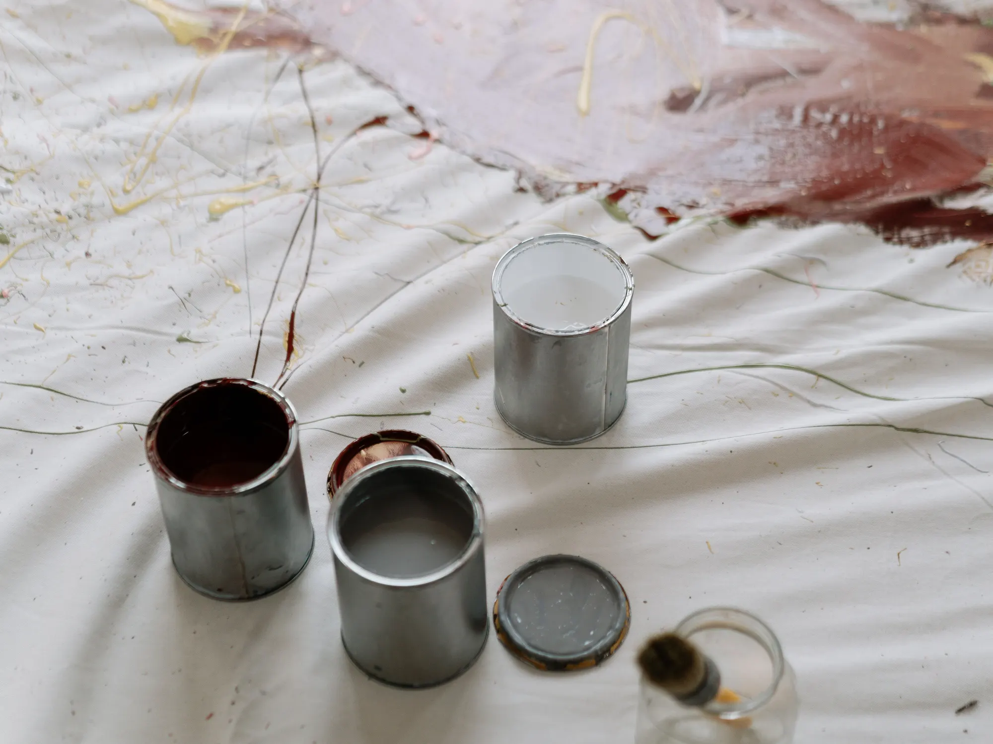 Open paint cans and a lid on a paint splattered white drop cloth