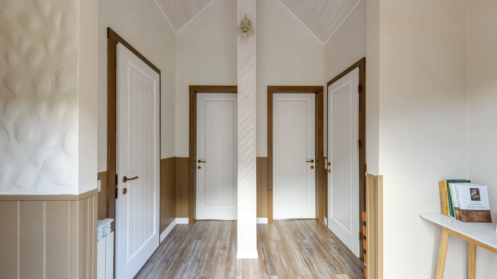 A short hallway with three white doors in wood casings, white walls above wood wainscot and a wood floor