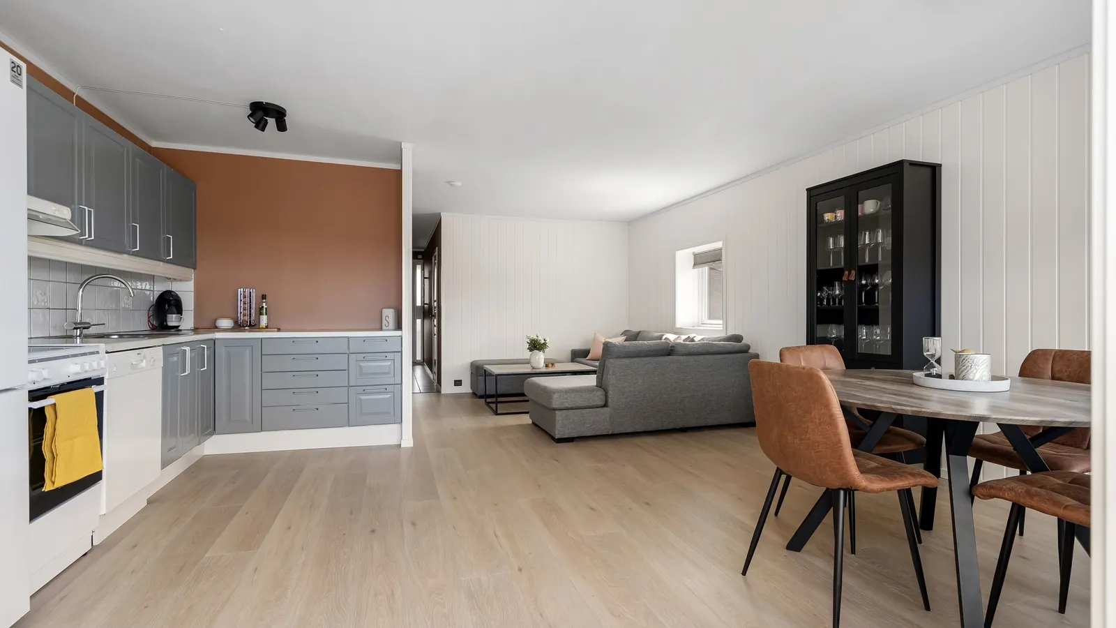 An open kitchen with gray cabinets and a terracotta accent wall running into a living area with a gray sofa and a dining table