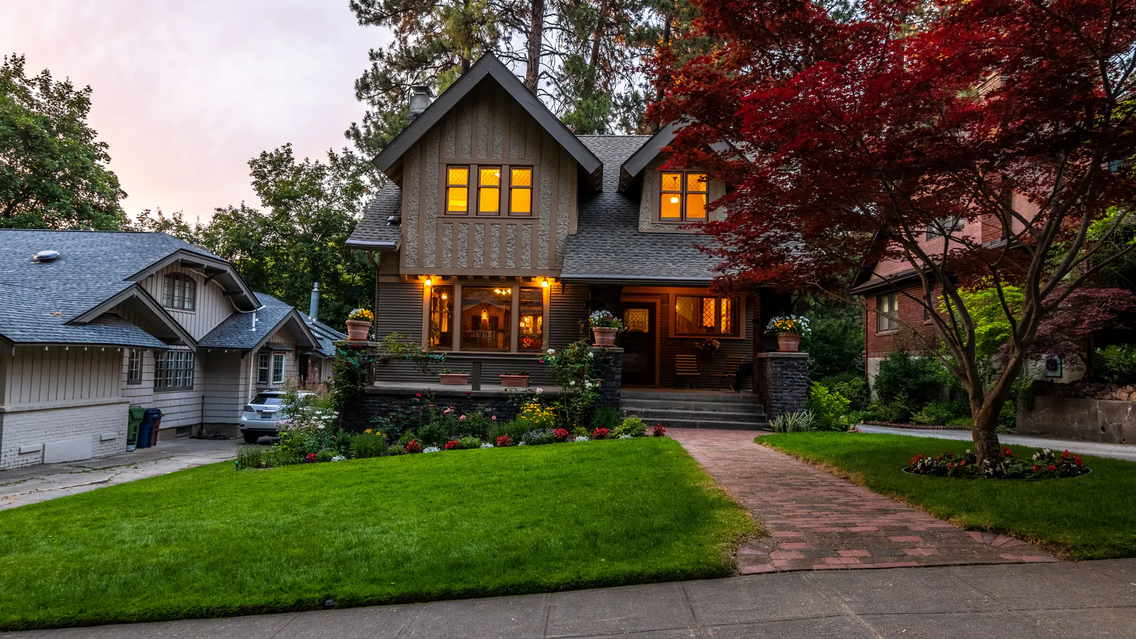 A two story shingle house at dusk behind a lawn