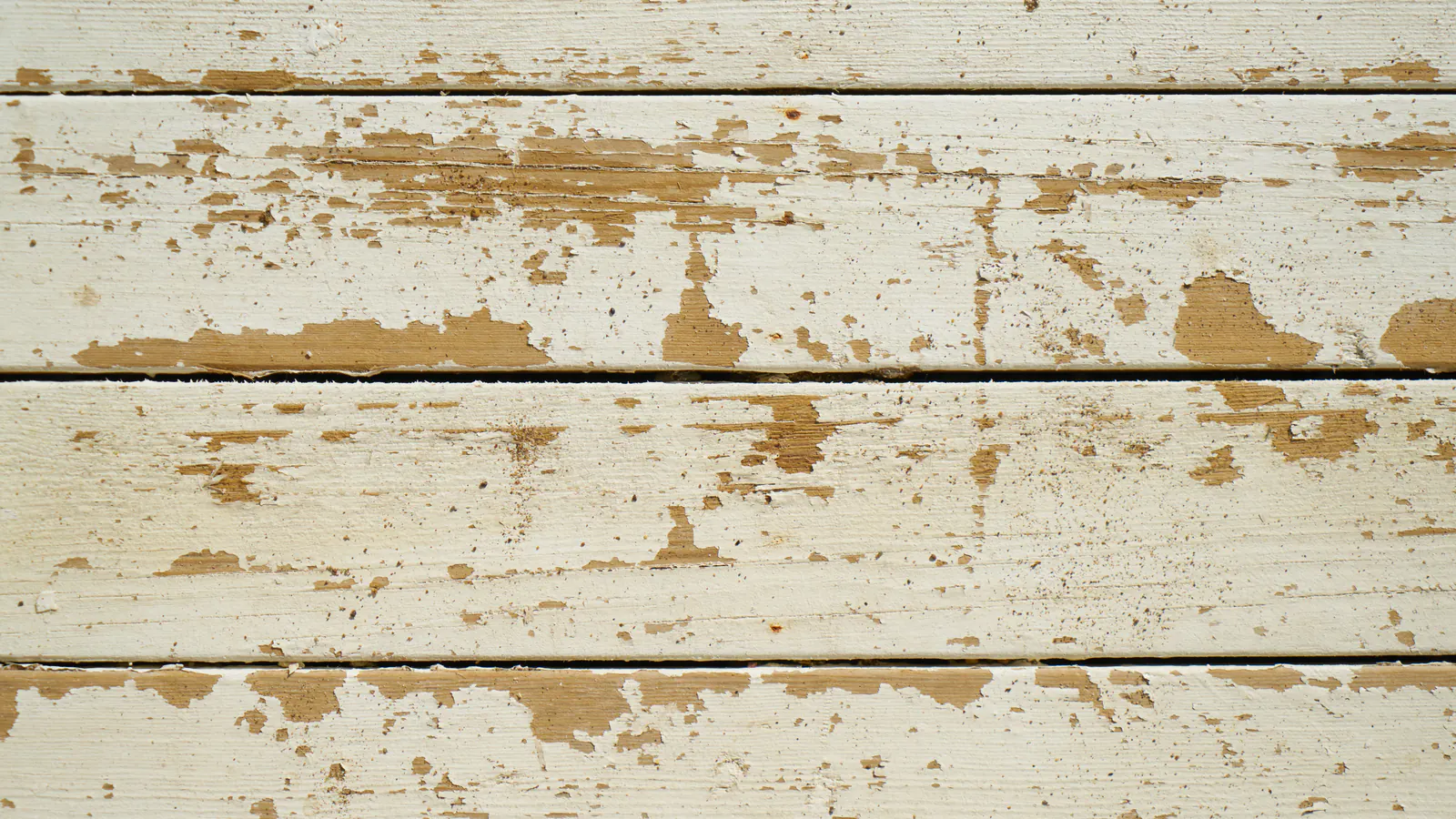 Horizontal wood boards with white paint flaking away in patches, showing bare tan wood underneath.