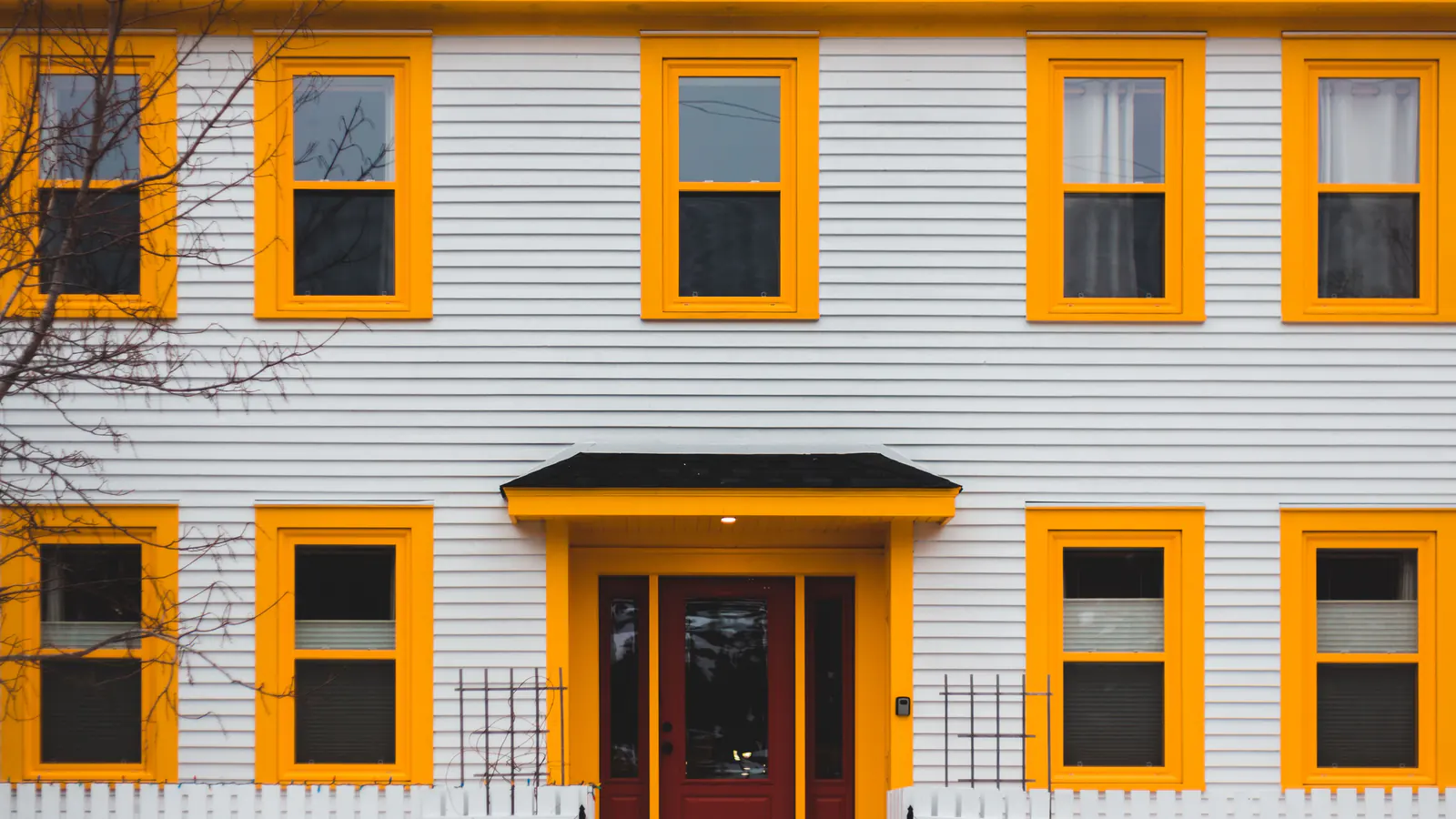 White siding with yellow window trim and a red front door