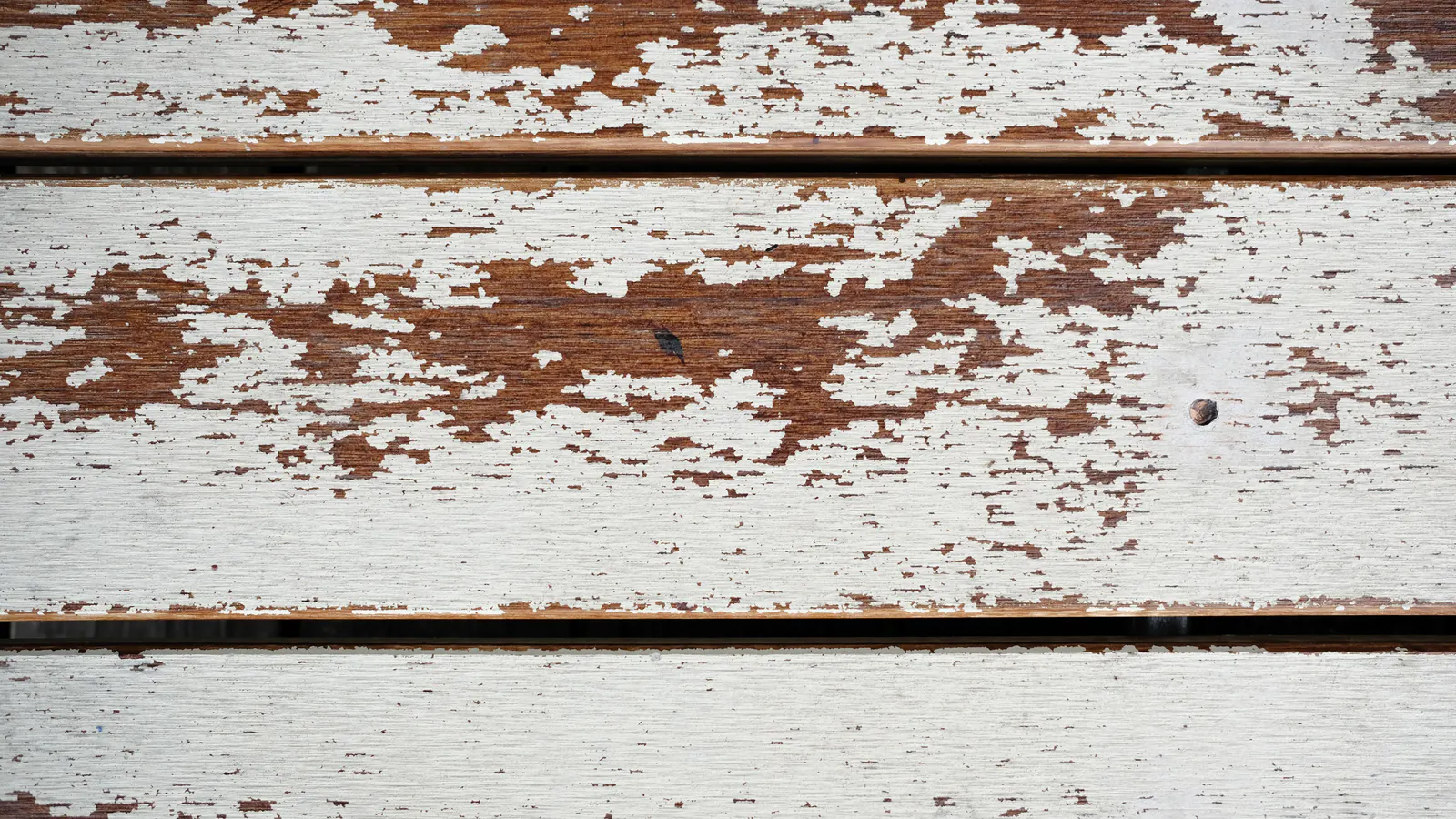 Horizontal wood boards with old white paint cracked and flaking away, exposing brown weathered wood beneath