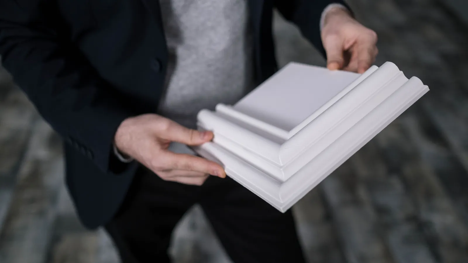 Two hands holding short lengths of white crown molding, showing the profile, with the person cropped at the shoulders.