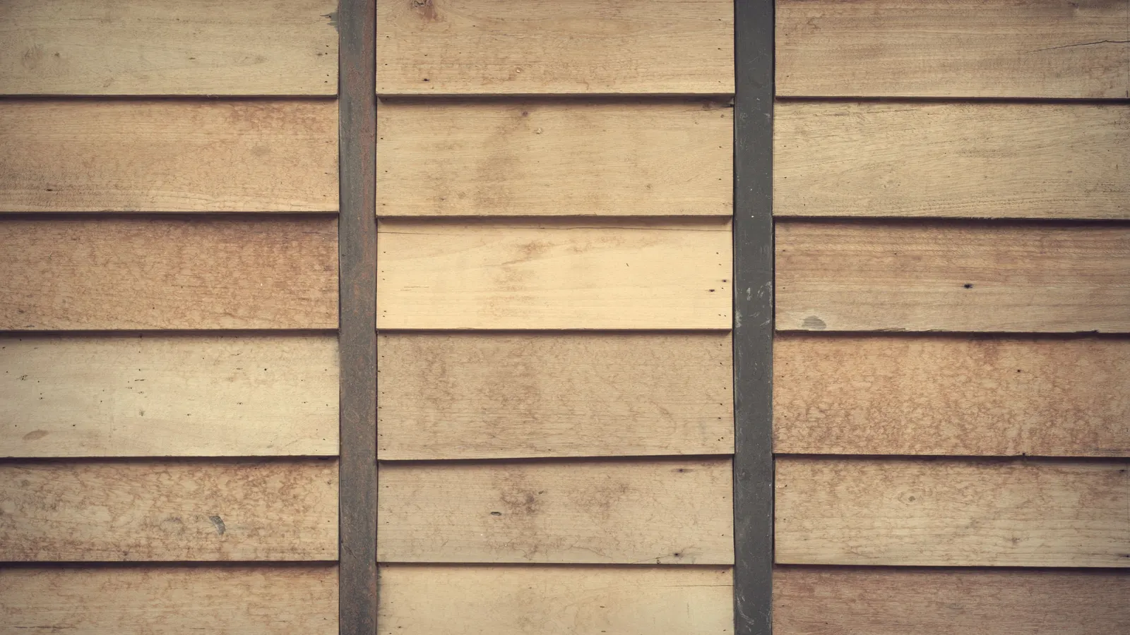 Close view of horizontal wood siding boards in tan and brown tones, divided by dark vertical battens