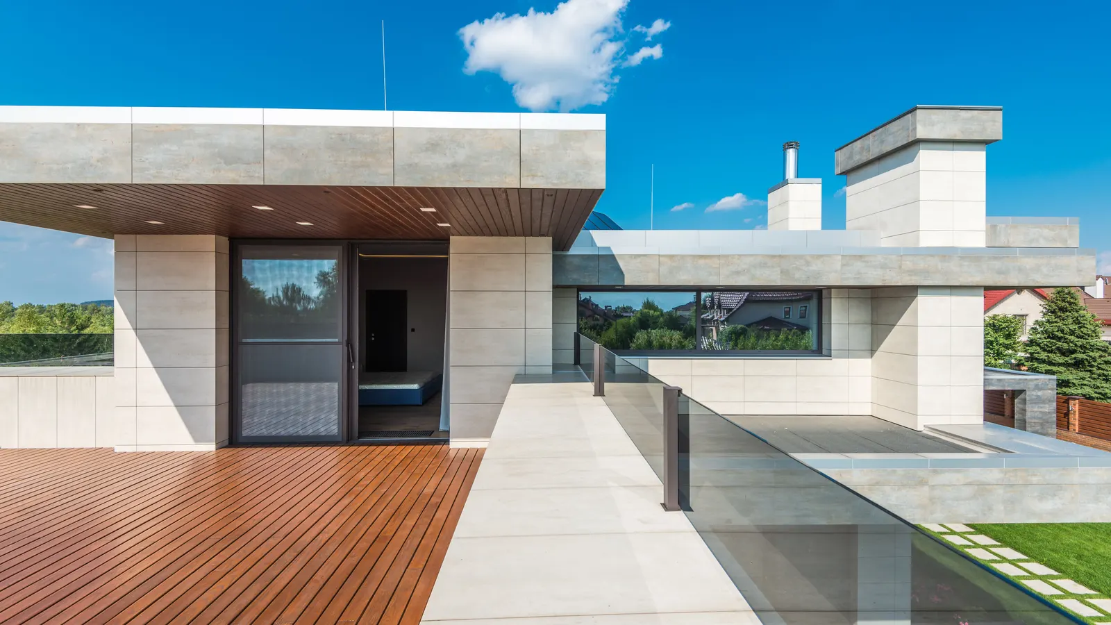 A reddish hardwood deck running along a modern white house with glass doors and a glass railing