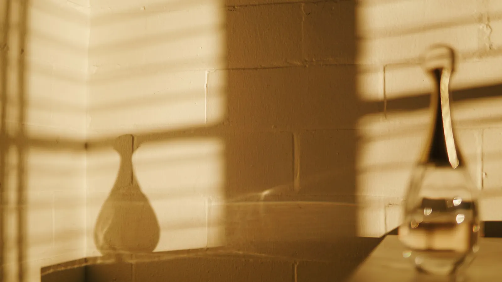 Warm low sunlight and window shadows falling across a painted block wall and a glass bottle