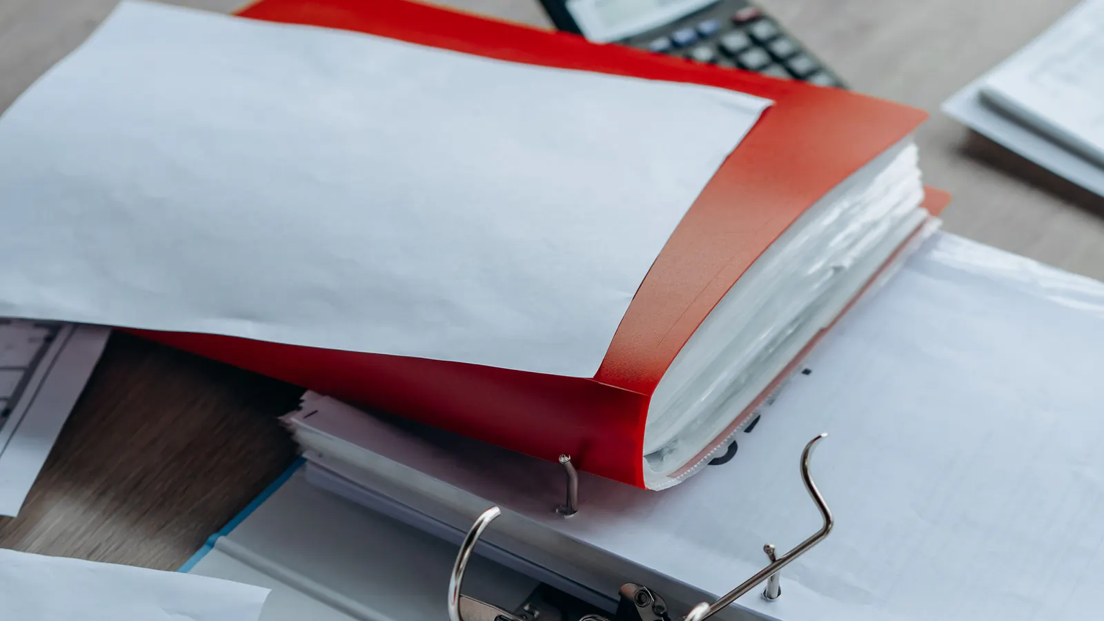 A red folder of papers resting on an open ring binder on a wooden desk