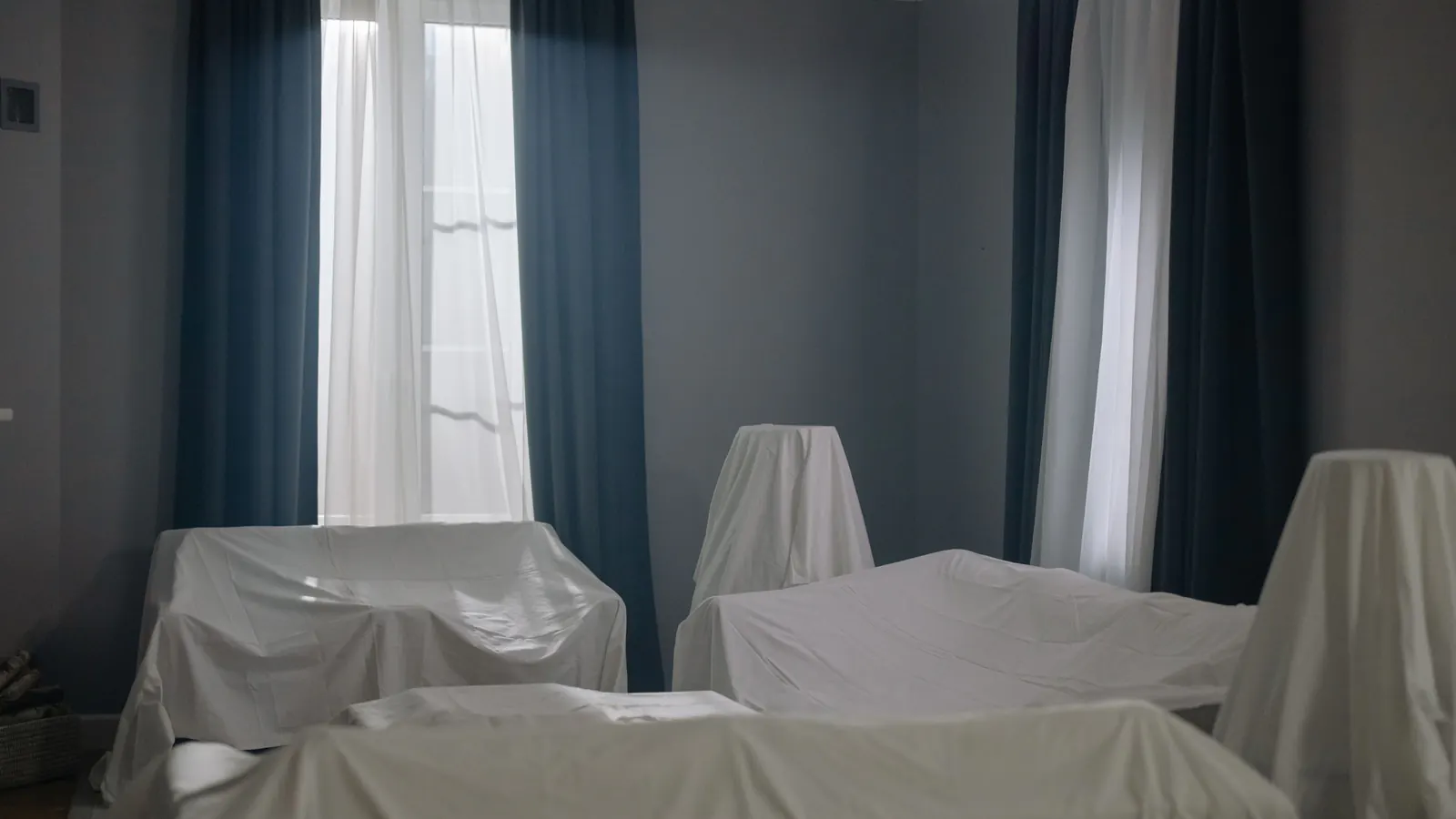 A room with its furniture covered in white sheets and the curtains drawn