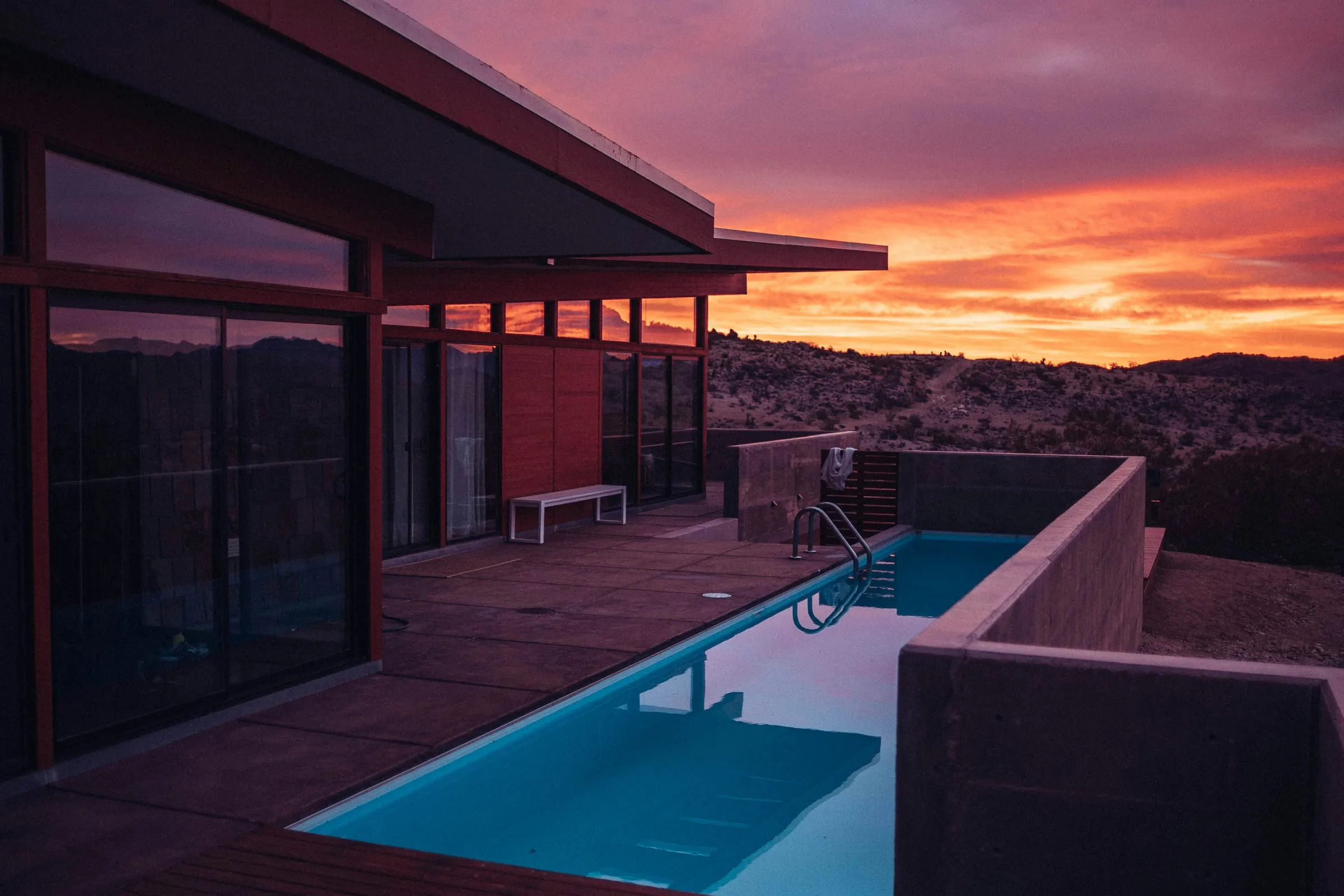 A modern house with a deck and a lap pool above the hills at sunset