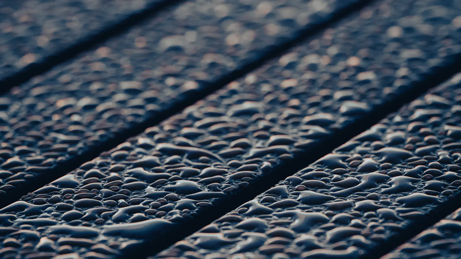 Rainwater beading on dark coated deck boards, close up
