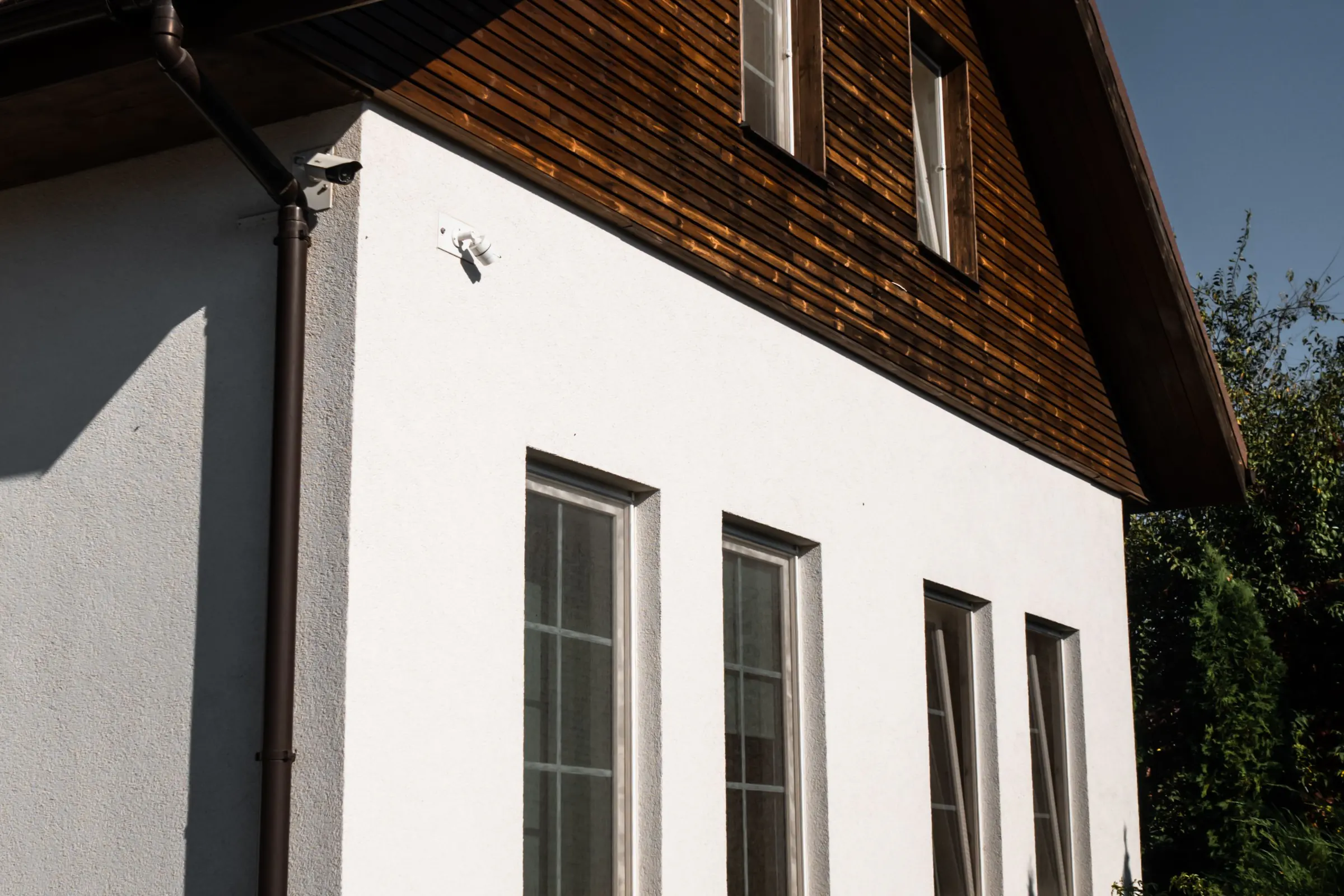 A white rendered house with a dark wood gable and white windows under a deep blue sky