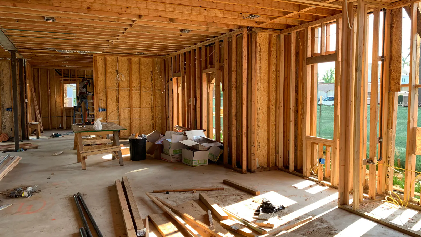 Sunlit interior with exposed wood wall studs, ceiling joists and window framing, lumber offcuts lying on the concrete floor