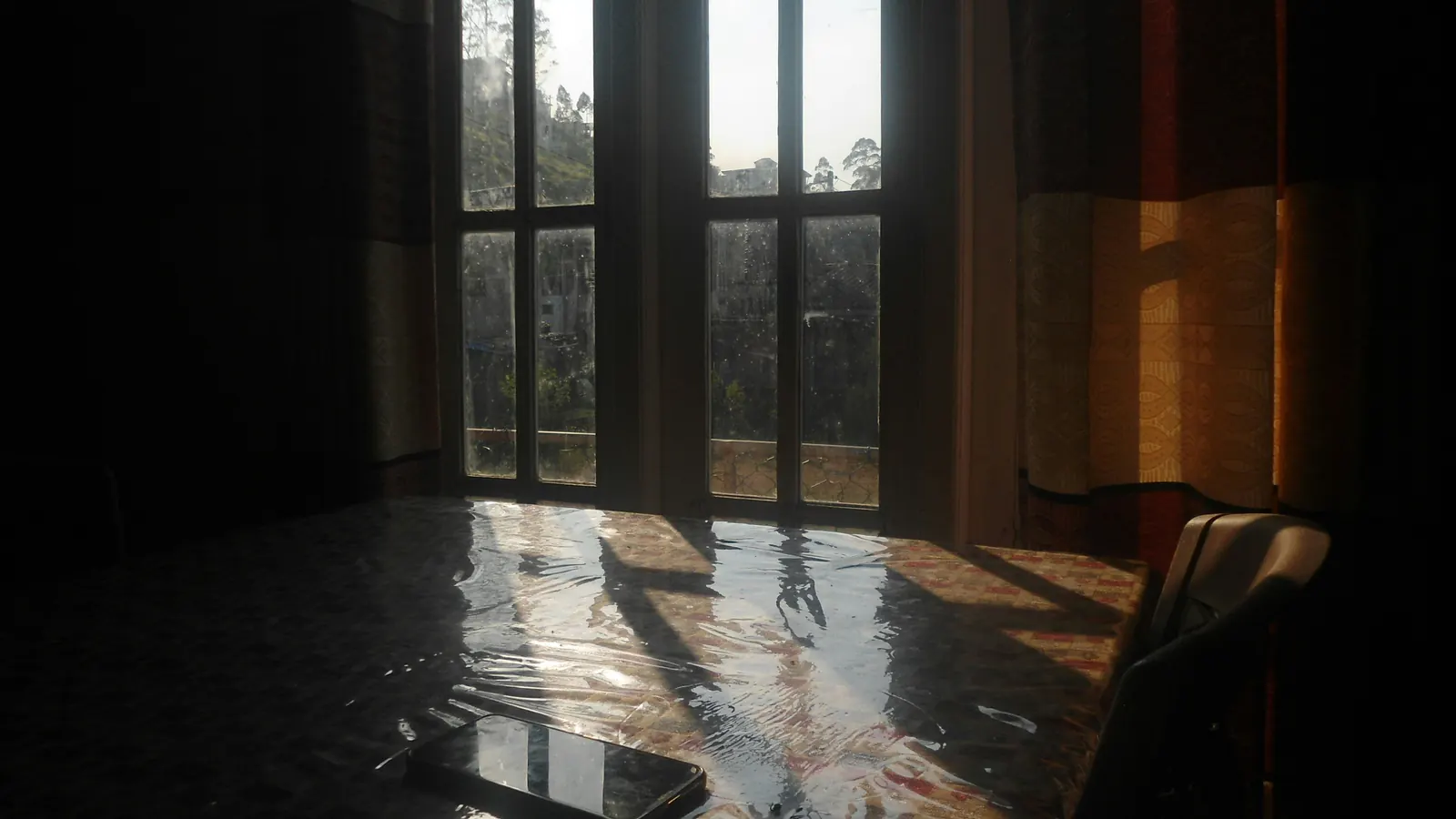 A shallow layer of standing water covering an indoor floor beside tall windows, with daylight reflecting across the wet surface
