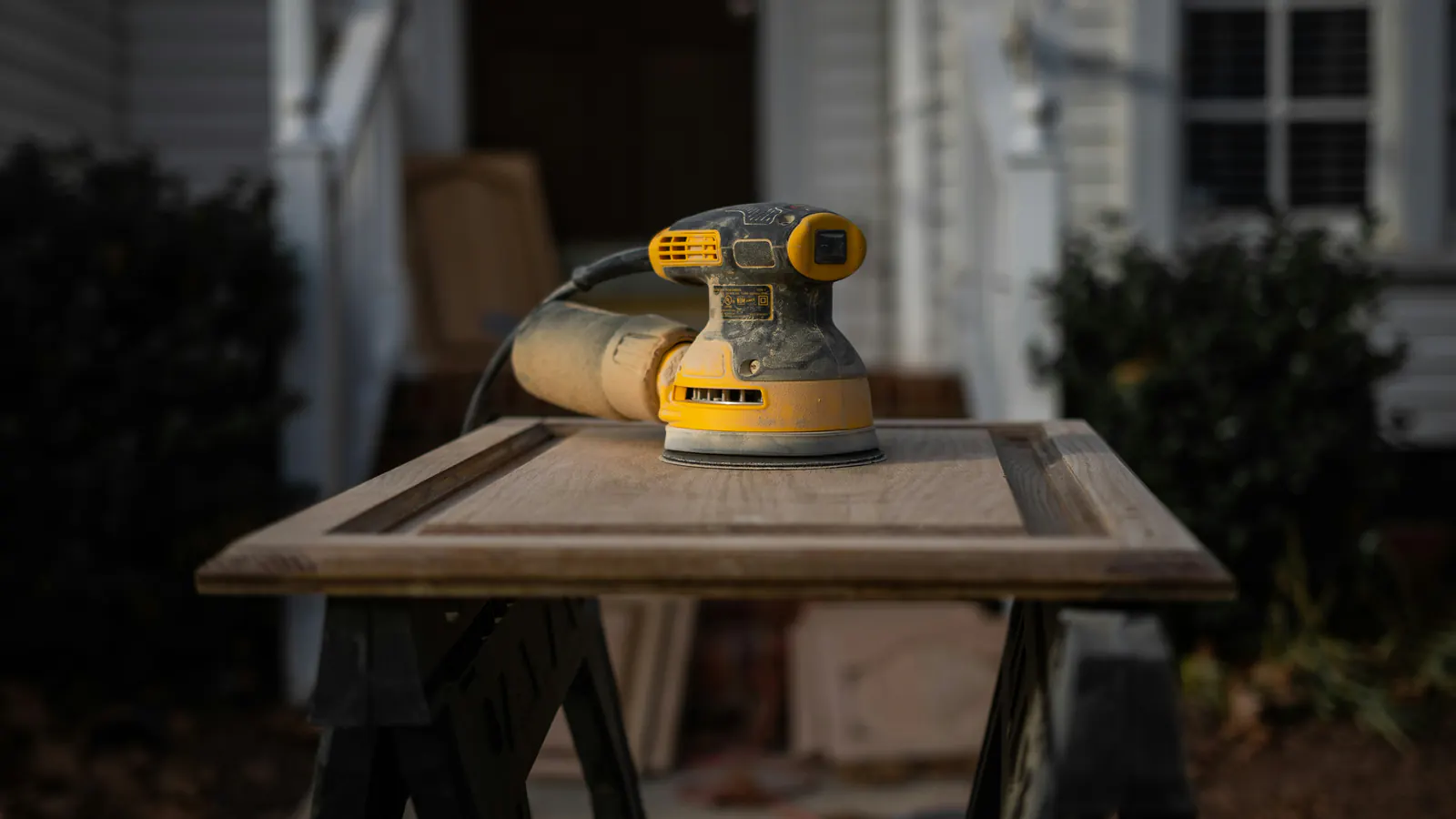 An orbital sander on a panel door laid across sawhorses