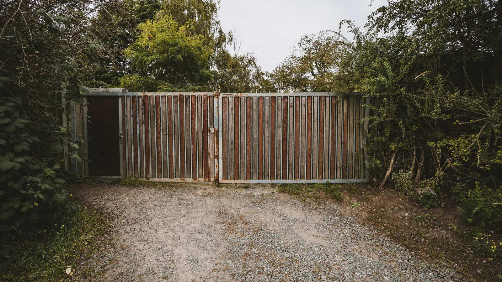 A closed wooden double gate at the end of a gravel drive, trees on both sides
