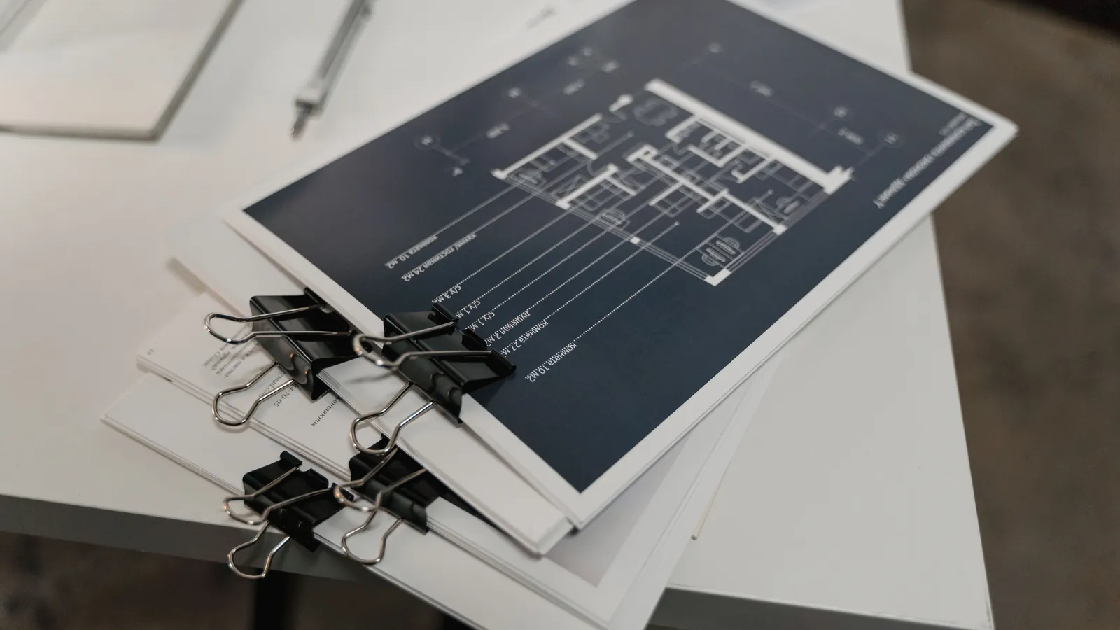 A stack of printed floor plans held with black binder clips on a white desk