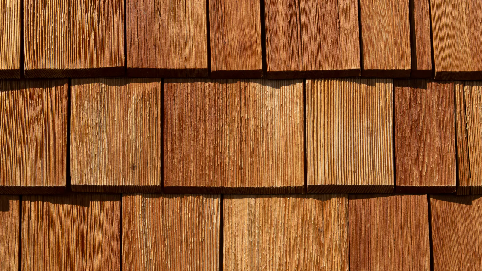 Close-up of fresh, unpainted cedar shingles in neat overlapping courses, showing warm orange-brown wood and textured grain