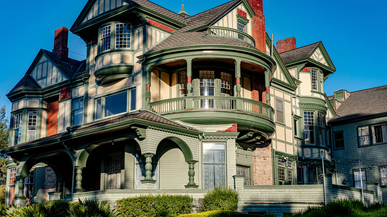 A Queen Anne Victorian house with a round corner tower, deep porches and green trim