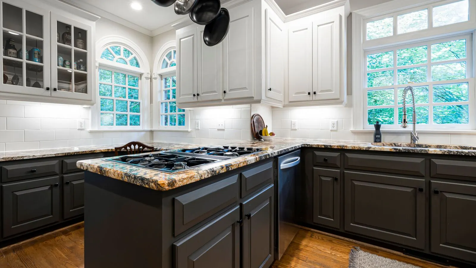 A kitchen with white painted upper cabinets, dark painted lower cabinets and island, granite counters and arched windows