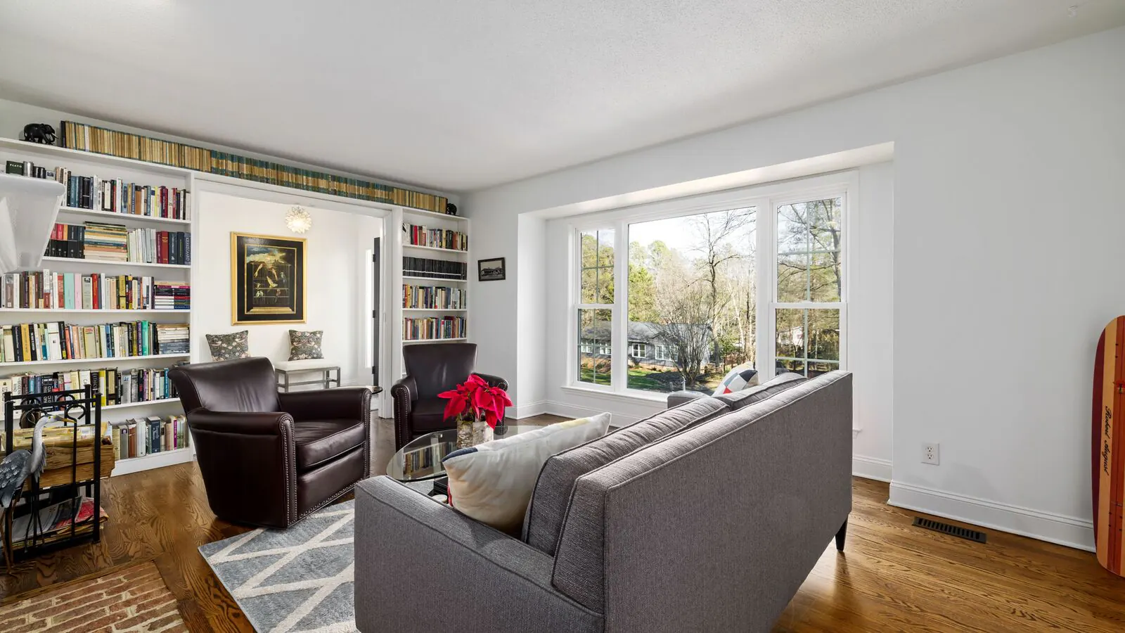 A living room with white walls, built-in bookshelves around a doorway, a gray sofa and a large window