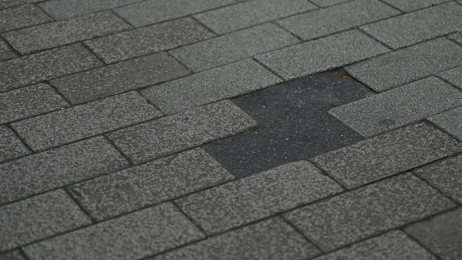 Grey asphalt shingle roof with a section of shingles missing or replaced, leaving a darker, mismatched patch in the middle of the courses.