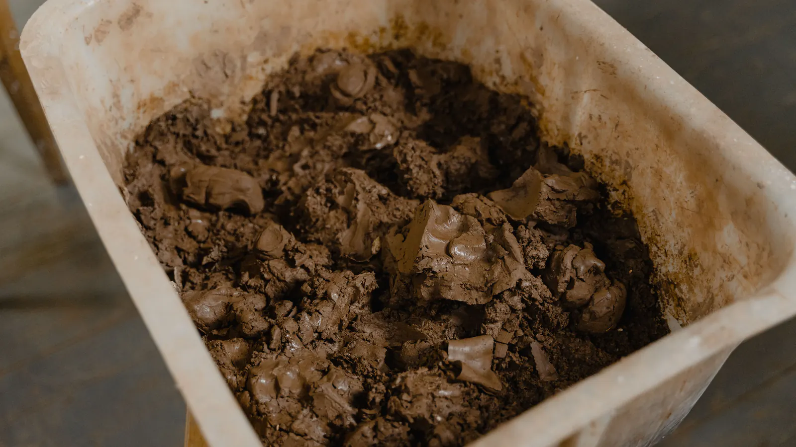 A scuffed white plastic tub filled with wet dark brown mud and sludge, sitting on a wooden floor