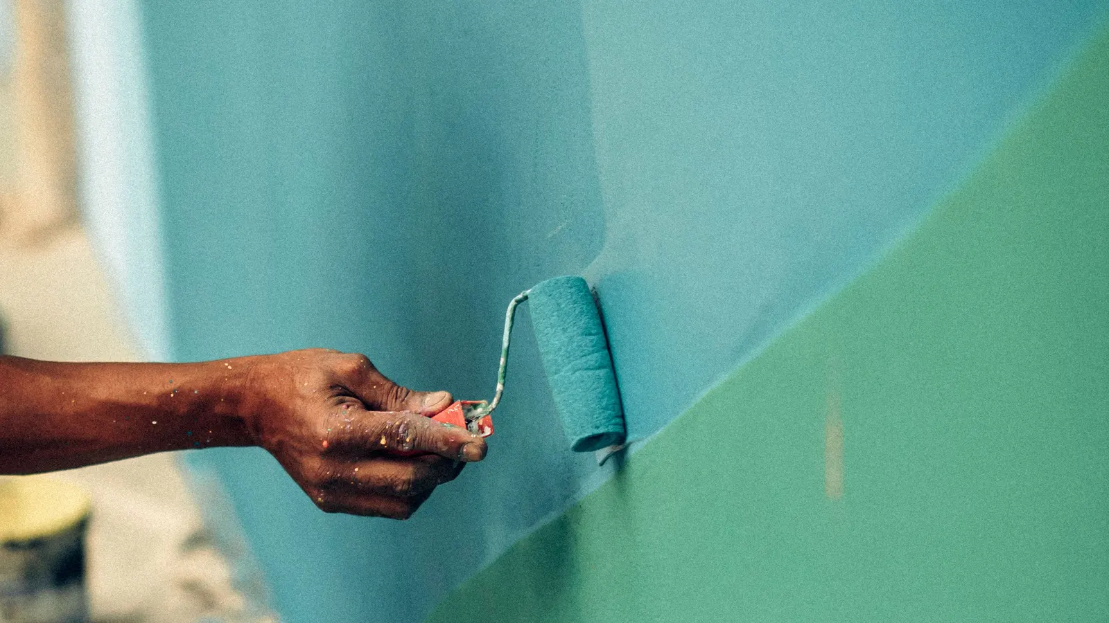 A roller putting green paint over a blue wall