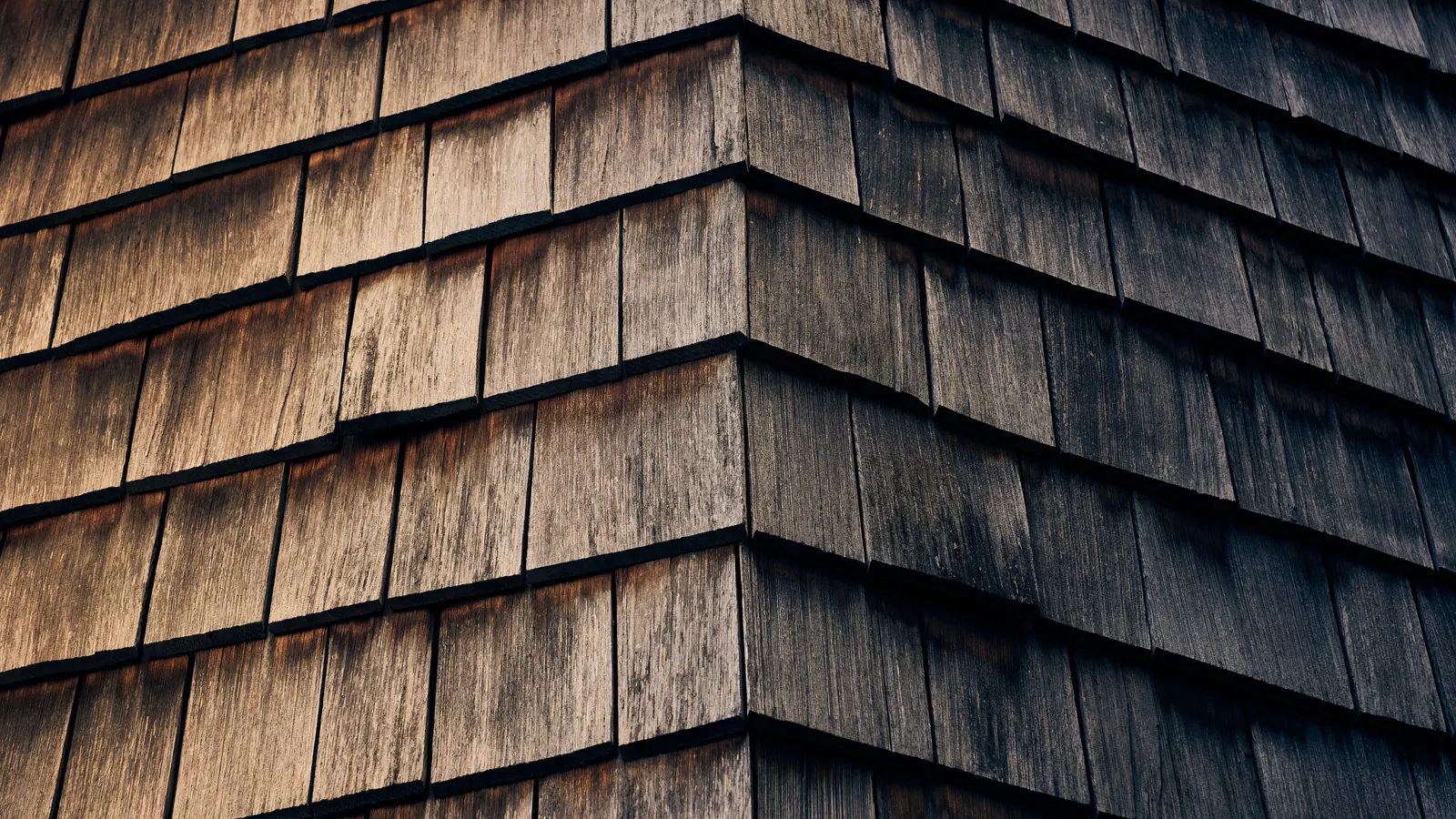 A corner of weathered cedar shingles with silvered, darkened faces and uneven color from long sun and weather exposure