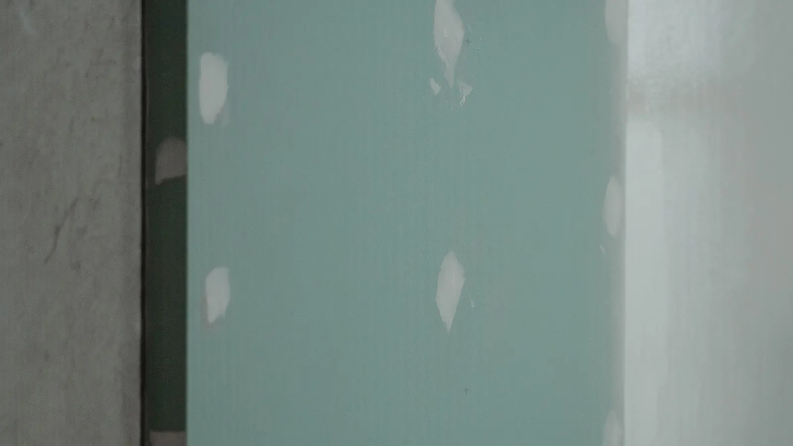 New green drywall with white spots of joint compound over the fasteners, before finishing