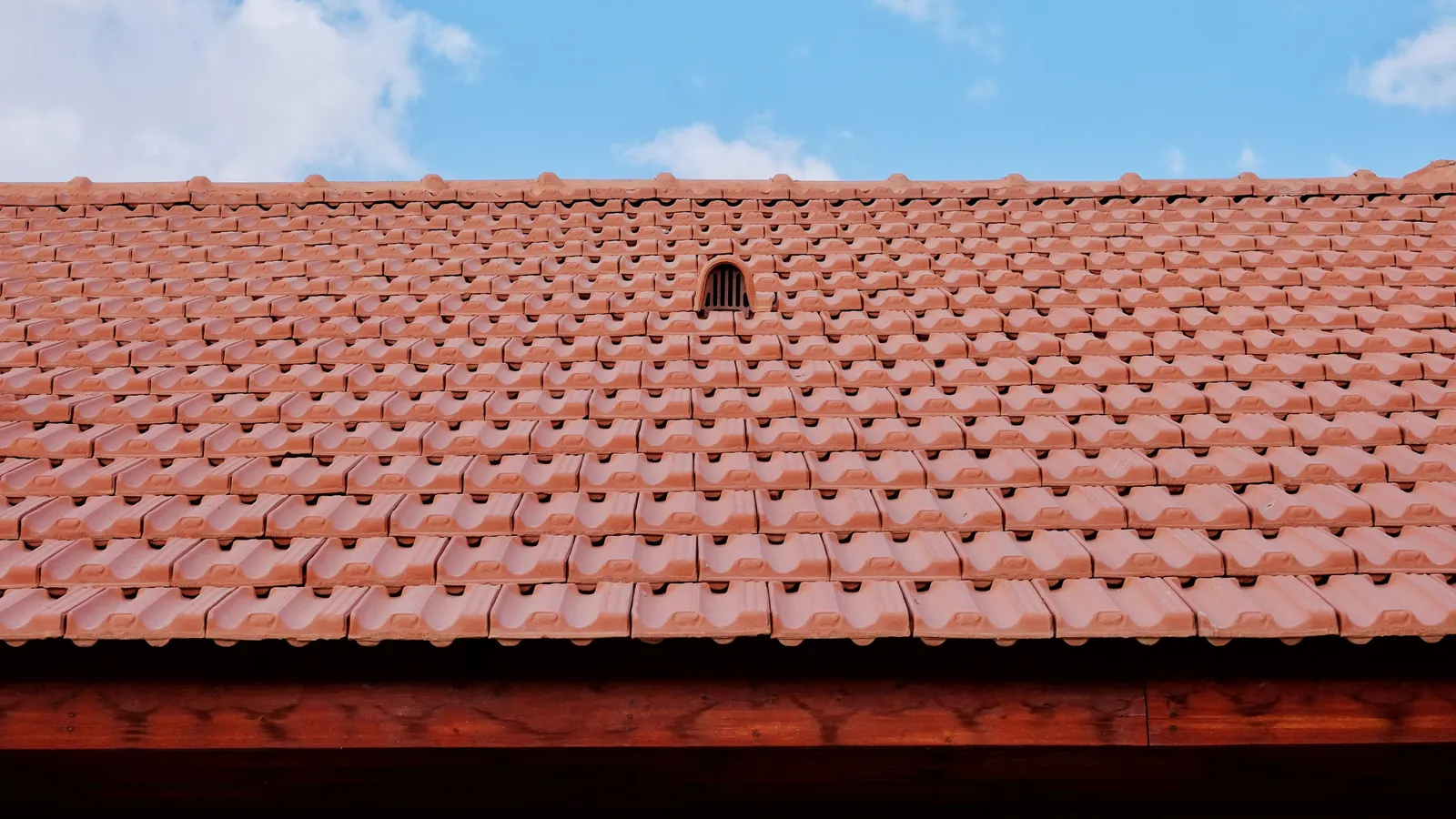 A clay tile roof with a small vent under a blue sky
