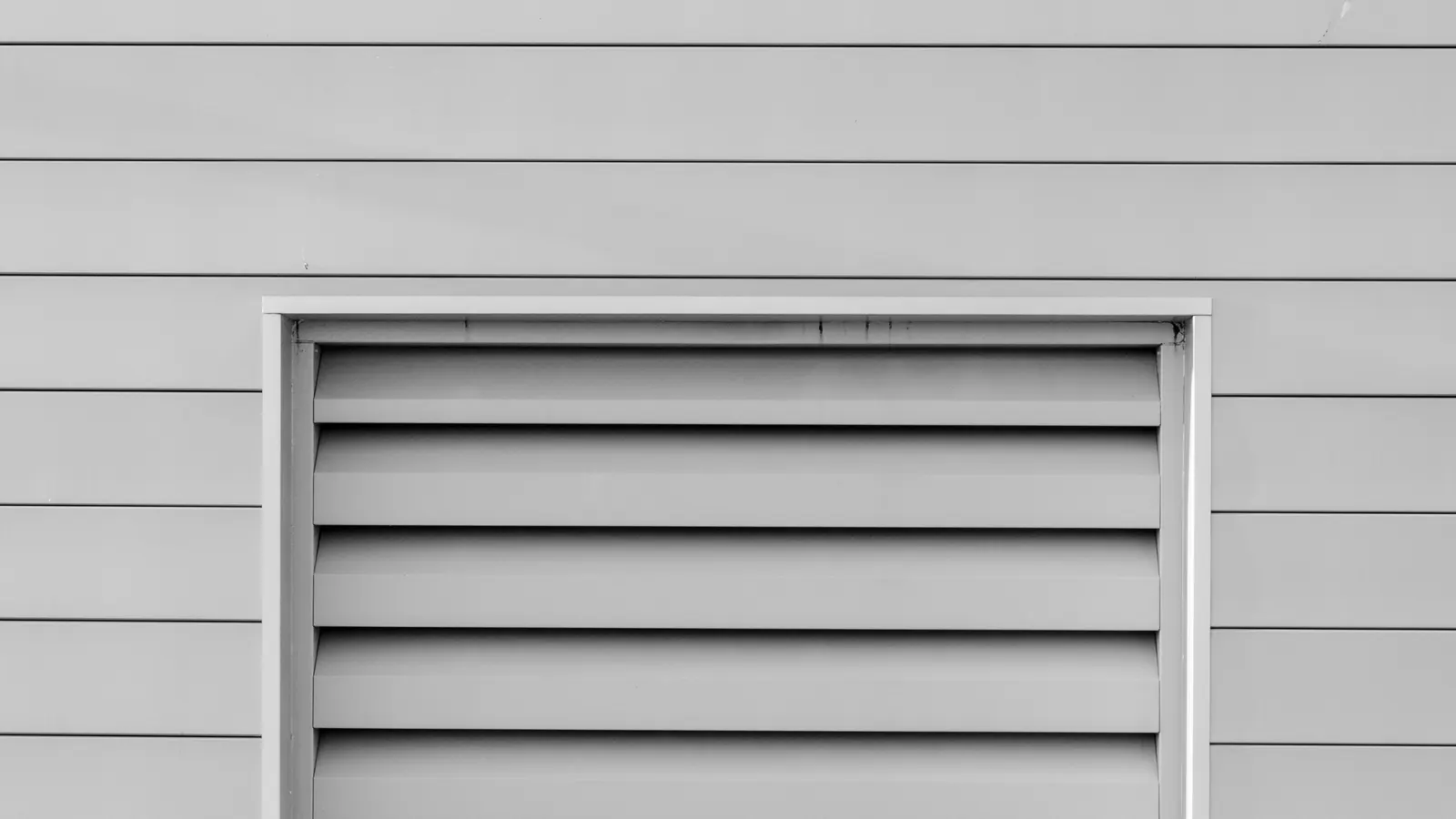 A louvered metal vent set into pale gray lap siding