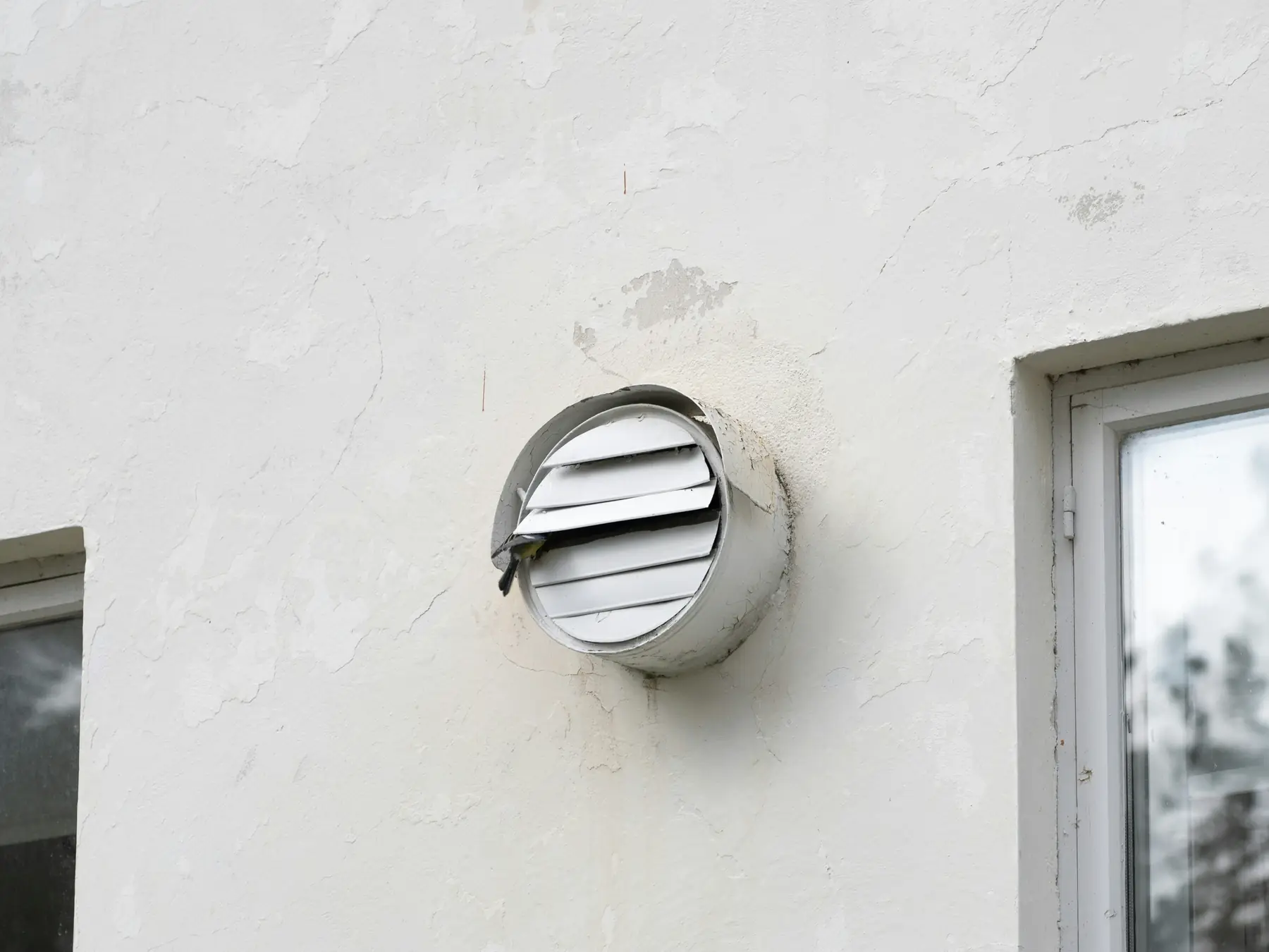 A round louvered vent on a white stucco wall, its slats bent