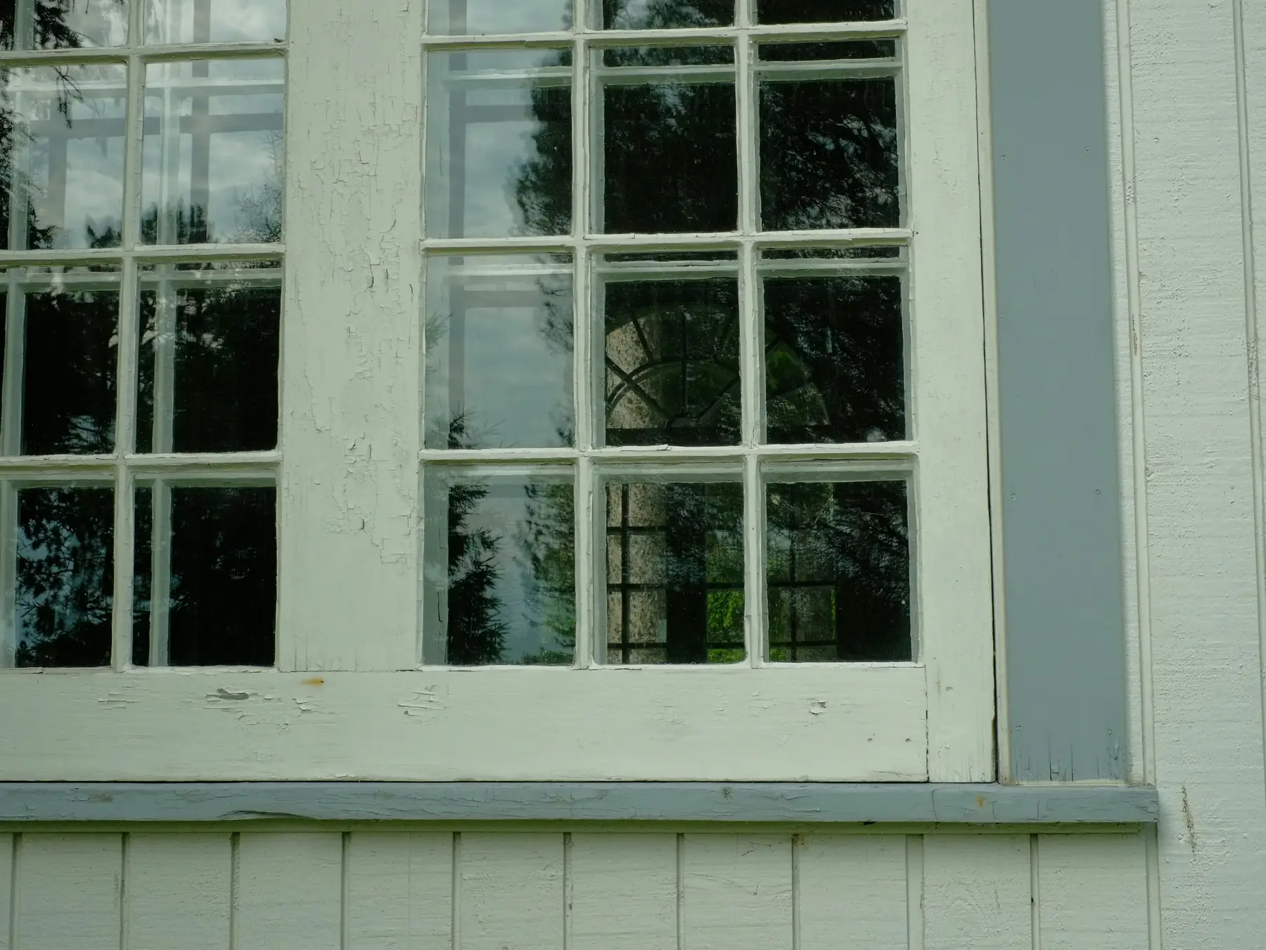 A white divided light window with cracked, flaking paint on the sash above the sill