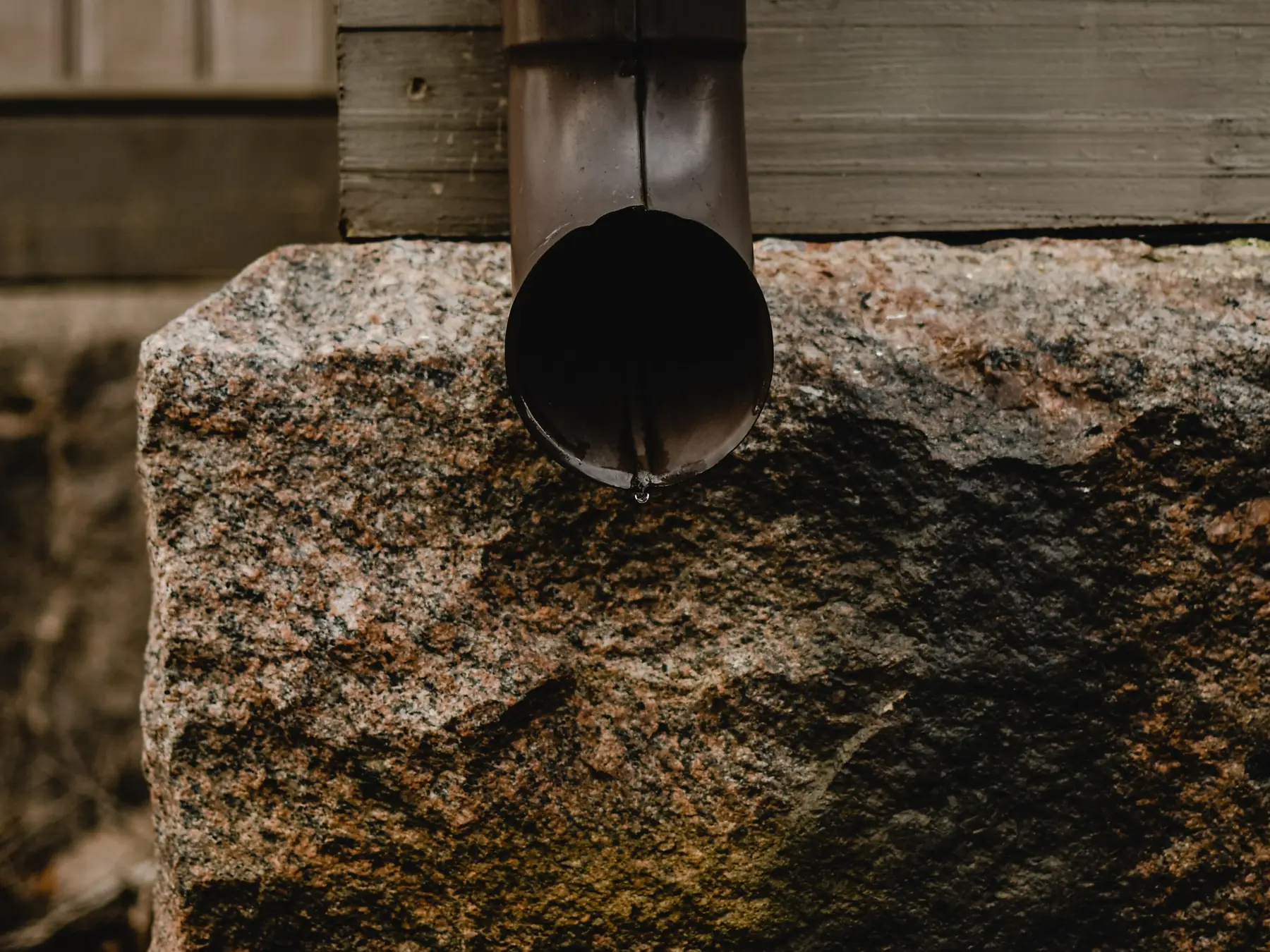 A brown metal downspout ending just above a rough granite block