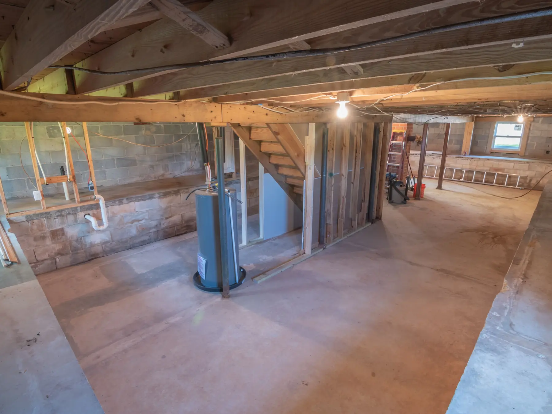 An unfinished basement with exposed joists, a water heater, pipes and a concrete floor