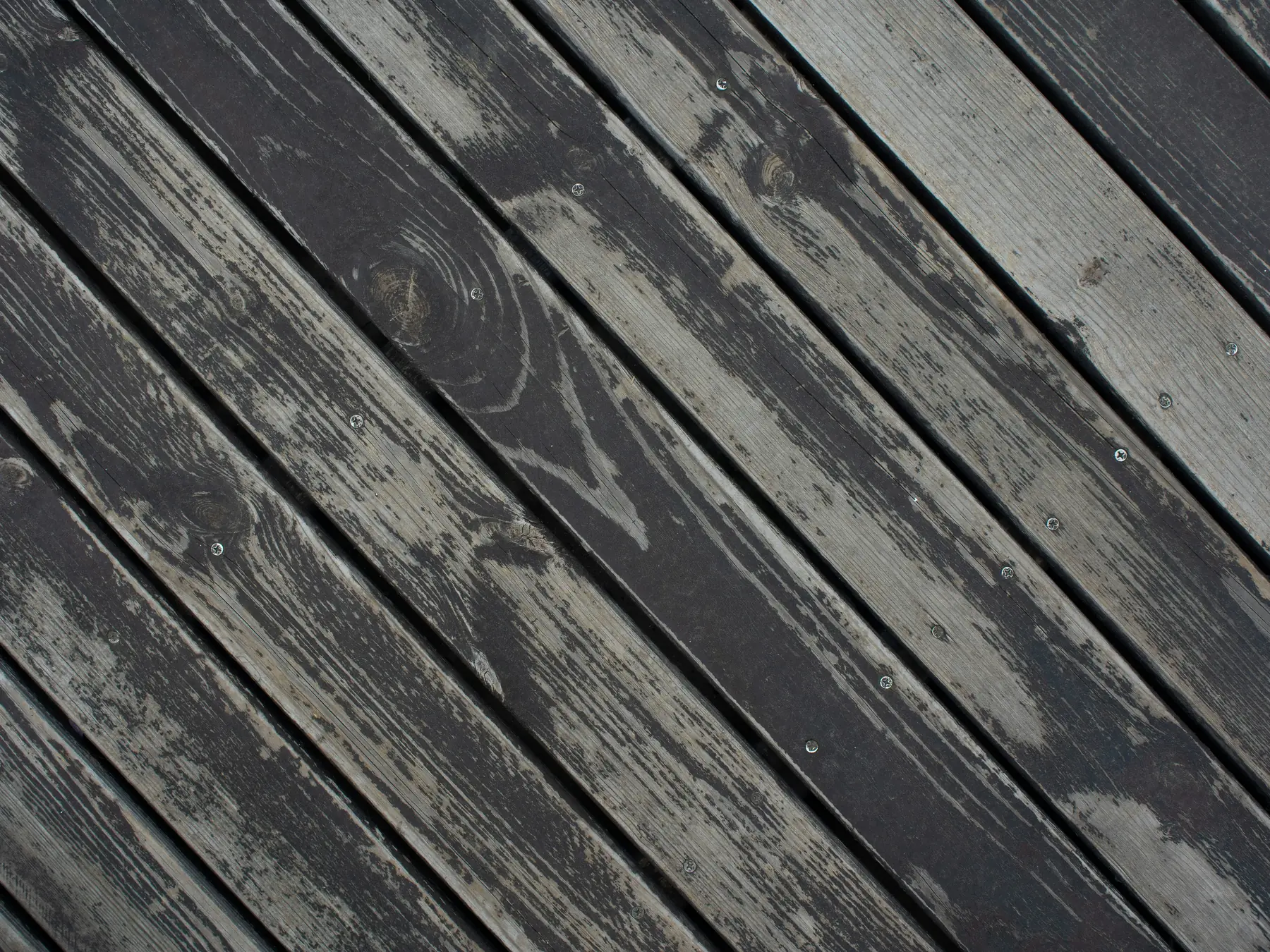 Diagonal deck boards with dark stain worn through to bare gray wood