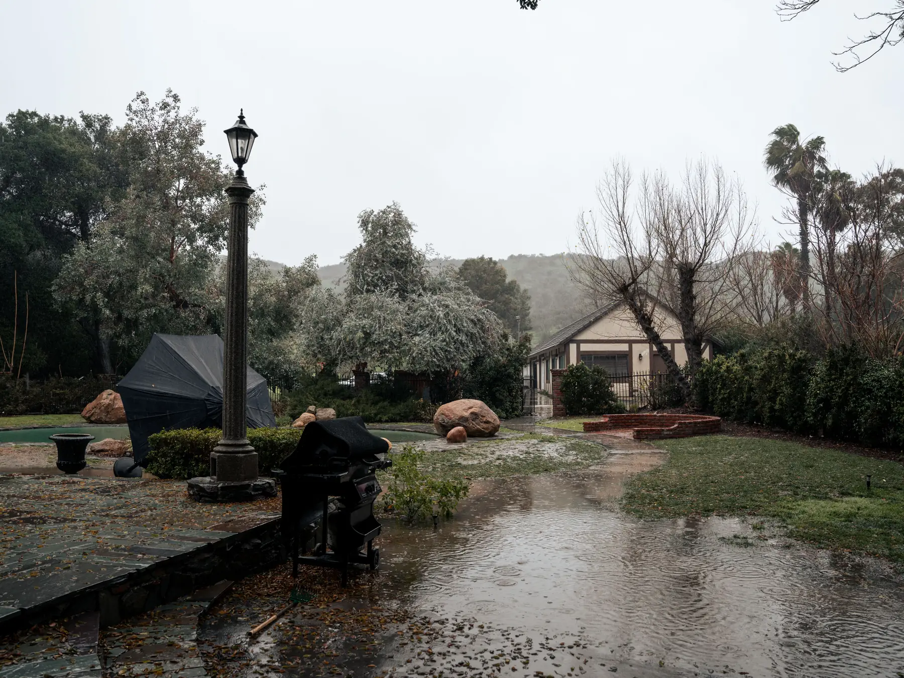 A backyard in heavy rain, water pooling across the lawn and patio