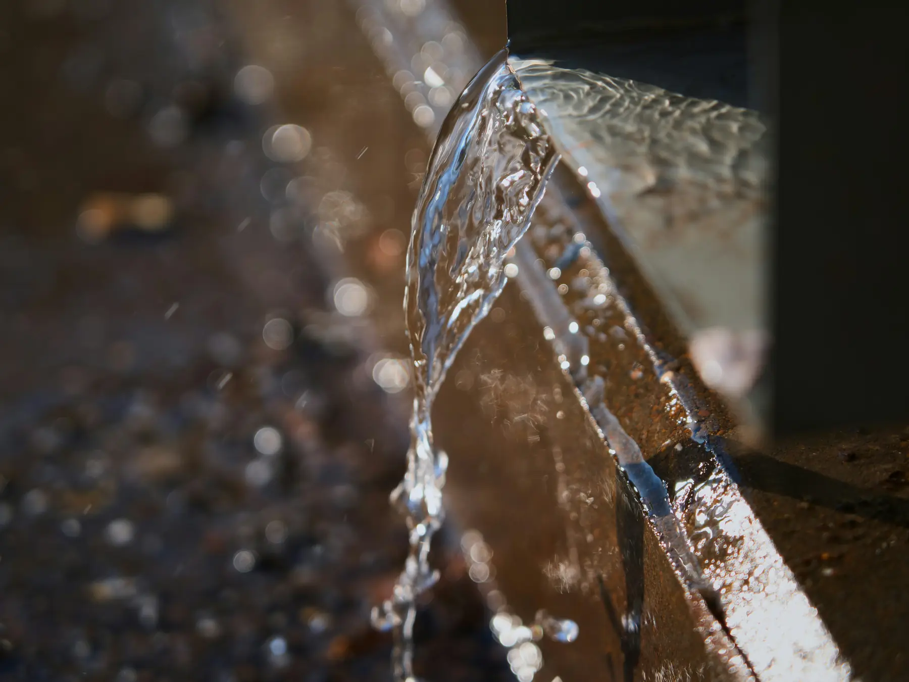 Water spilling from the open end of a pipe onto gravel in low sunlight