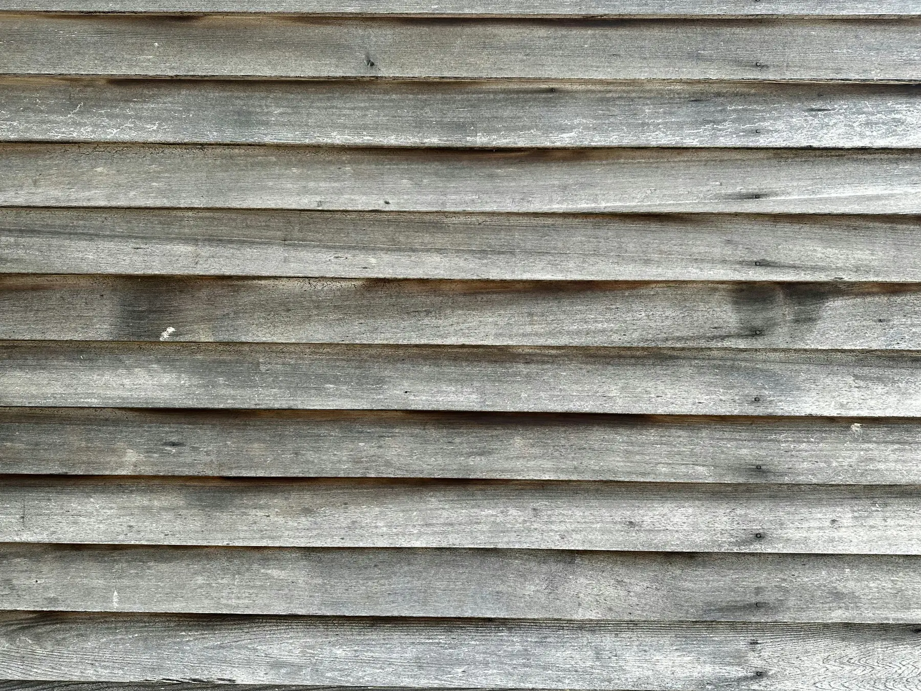 Gray weathered wood lap siding with dark water stains along the board edges