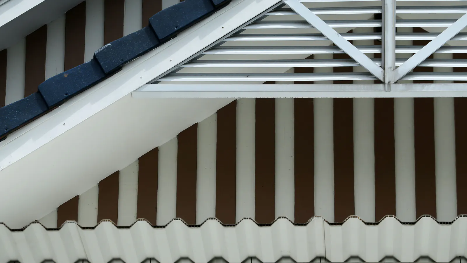 Close-up of a white gable trim and eave with dark roof shingles along the edge and slatted vents above striped siding