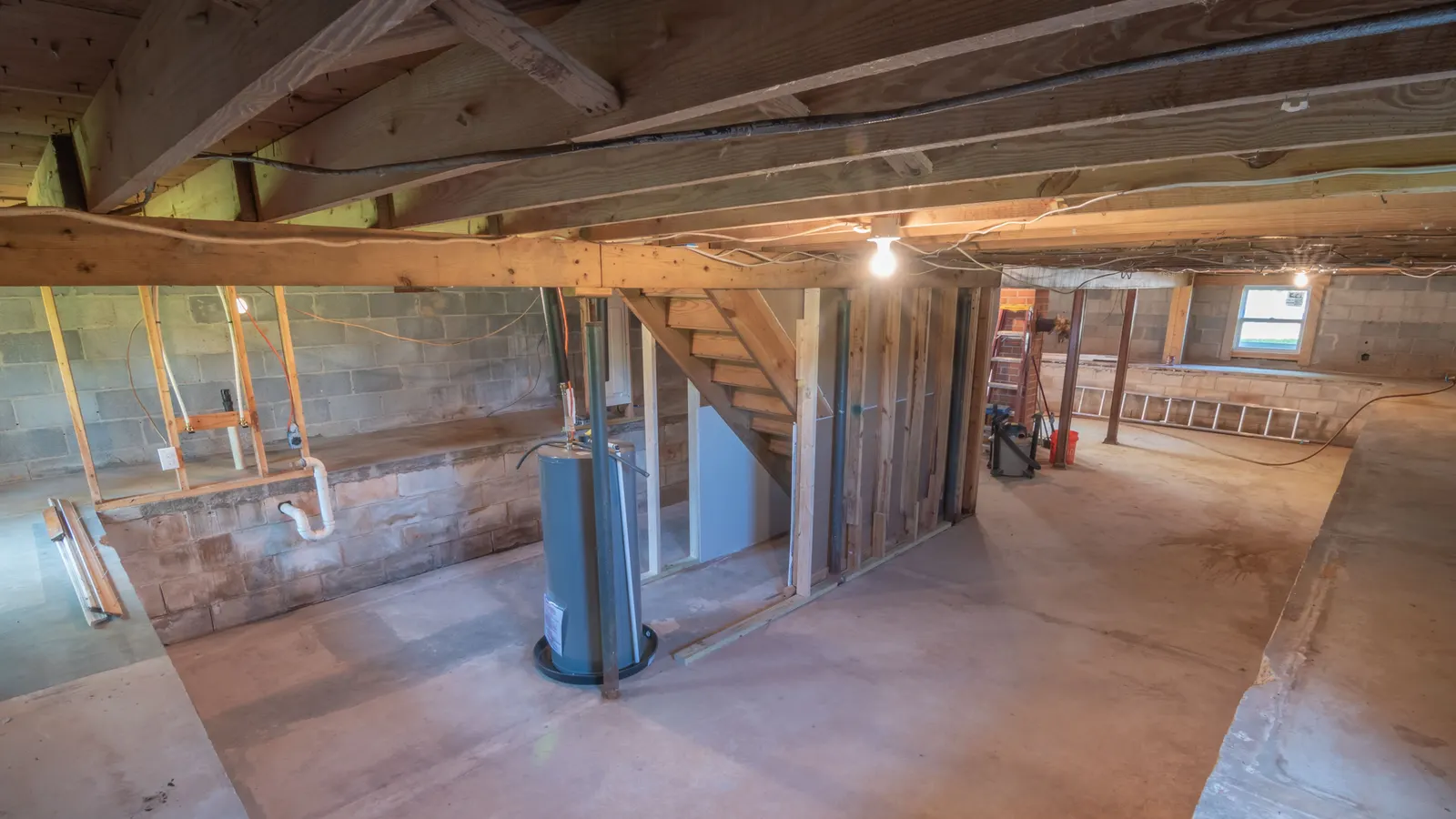 An unfinished basement with a water heater, exposed joists and pipes over a concrete floor