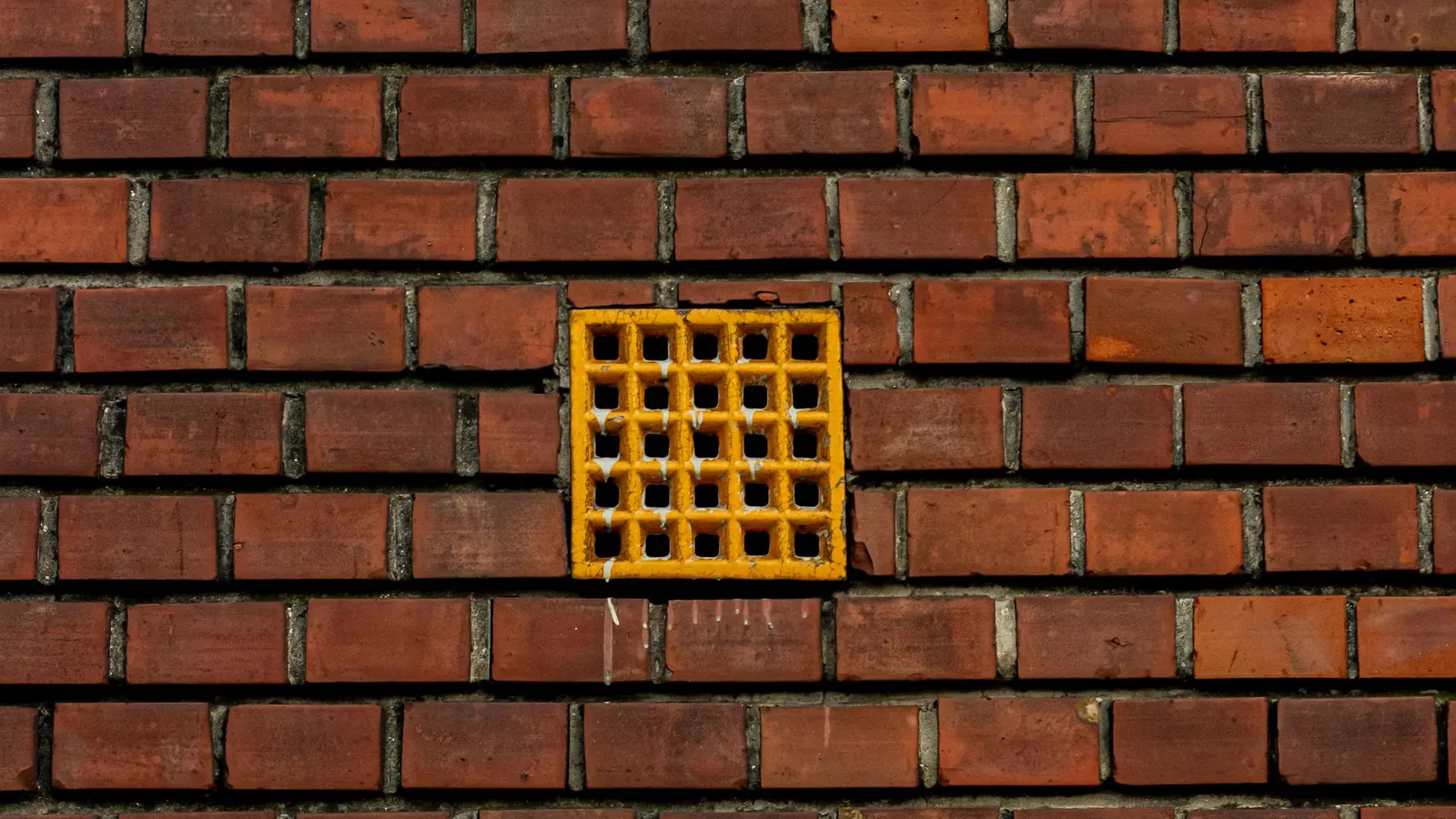 A small square yellow vent grate set into a red brick wall