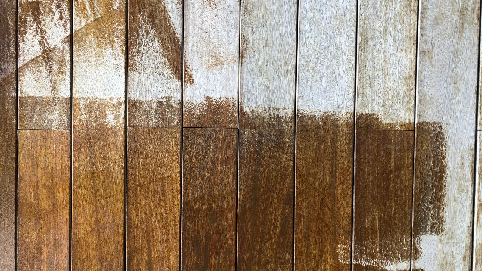 Vertical wood boards with a pale coat brushed over the upper part and rich brown wood showing below, brush strokes visible at the edge