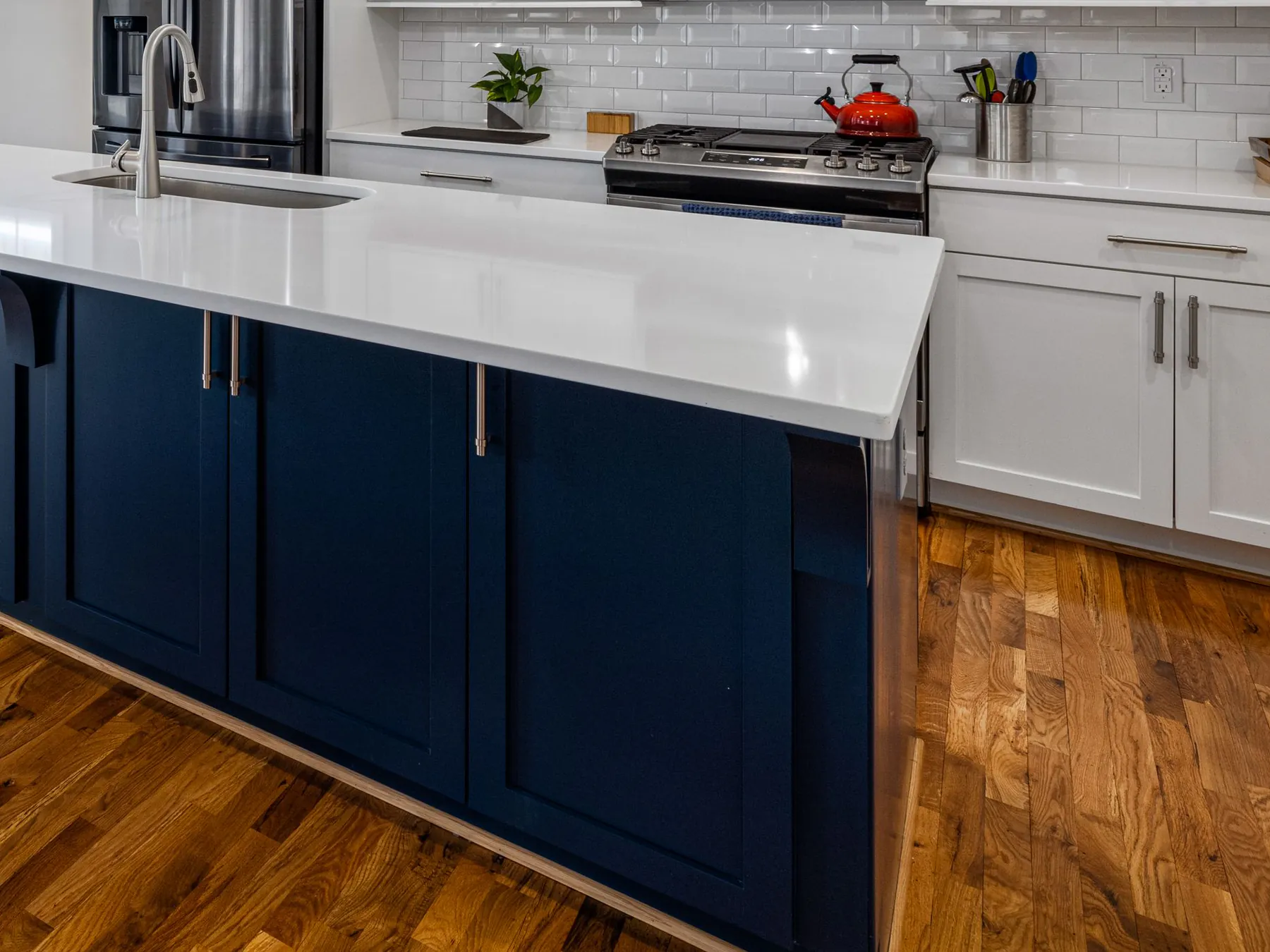 A navy painted kitchen island with a white counter beside white shaker cabinets on an oak floor