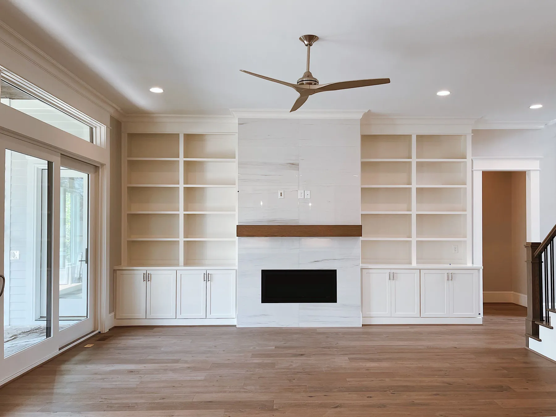 White built-in shelves and cabinets on both sides of a fireplace in an empty living room